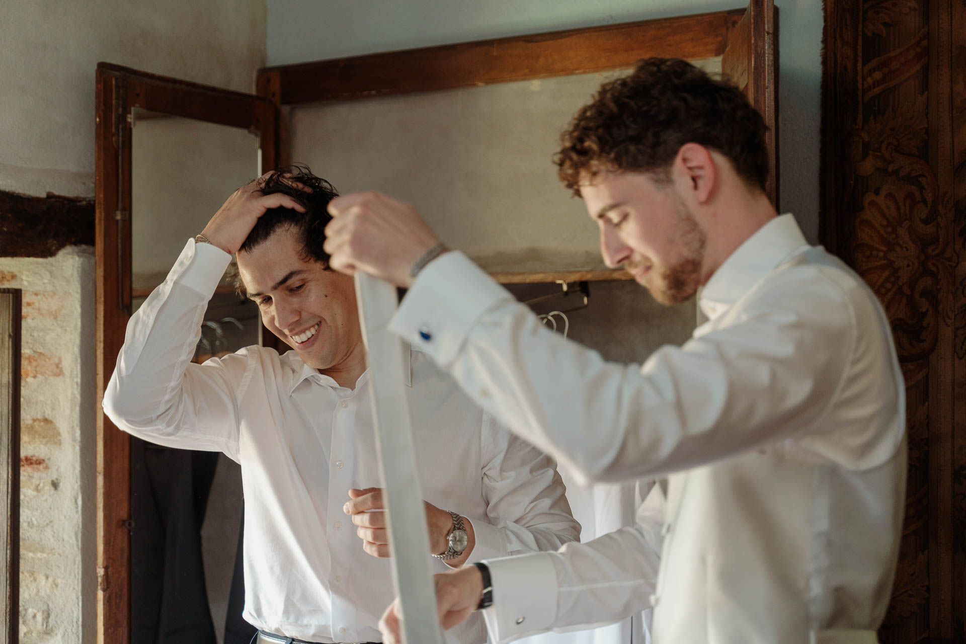 Lo sposo ride con la mano tra i capelli, mentre un amico gli passa la cravatta