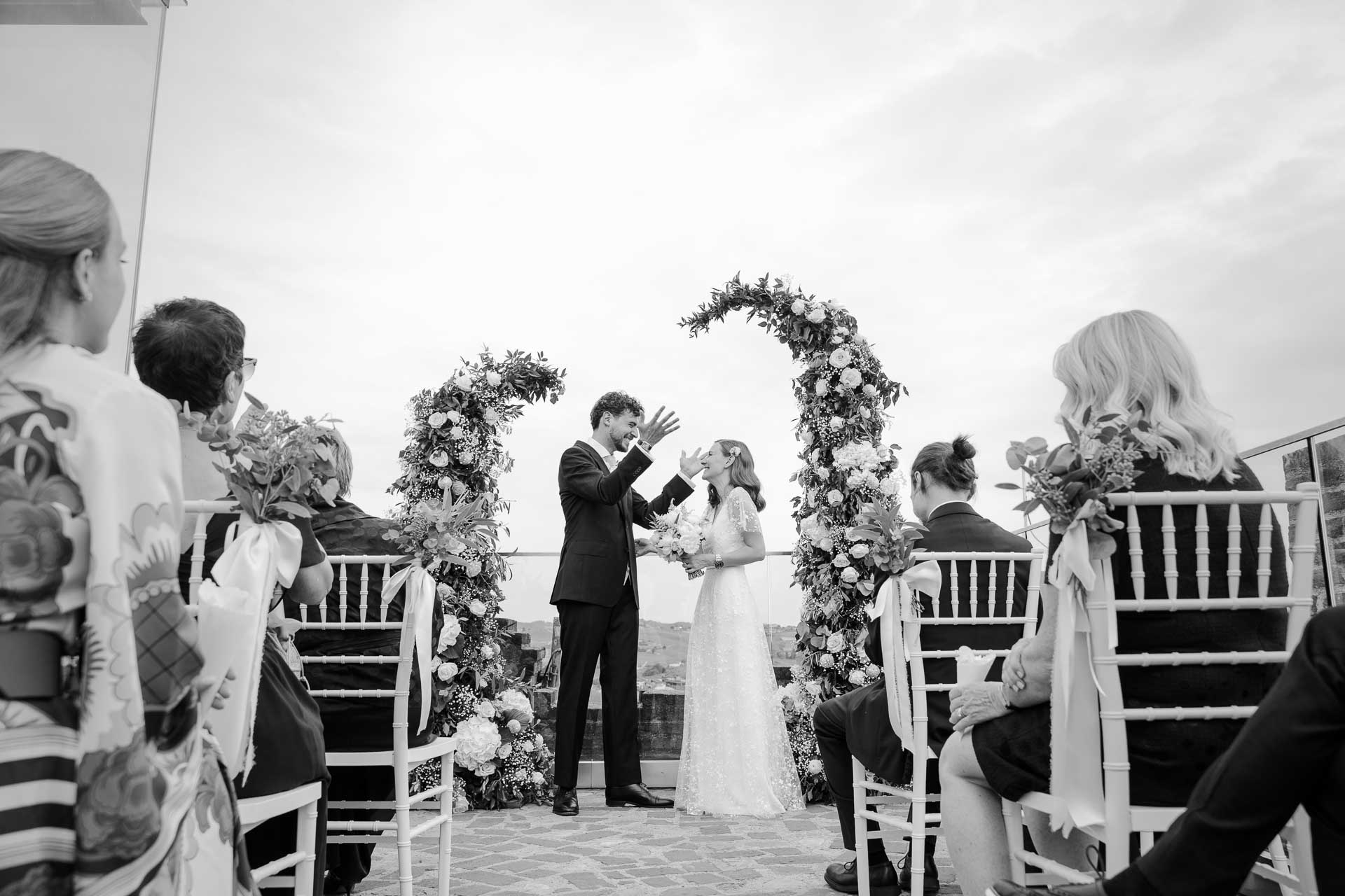 In bianco e nero, gli sposi alzano le braccia in festa tra gli invitati