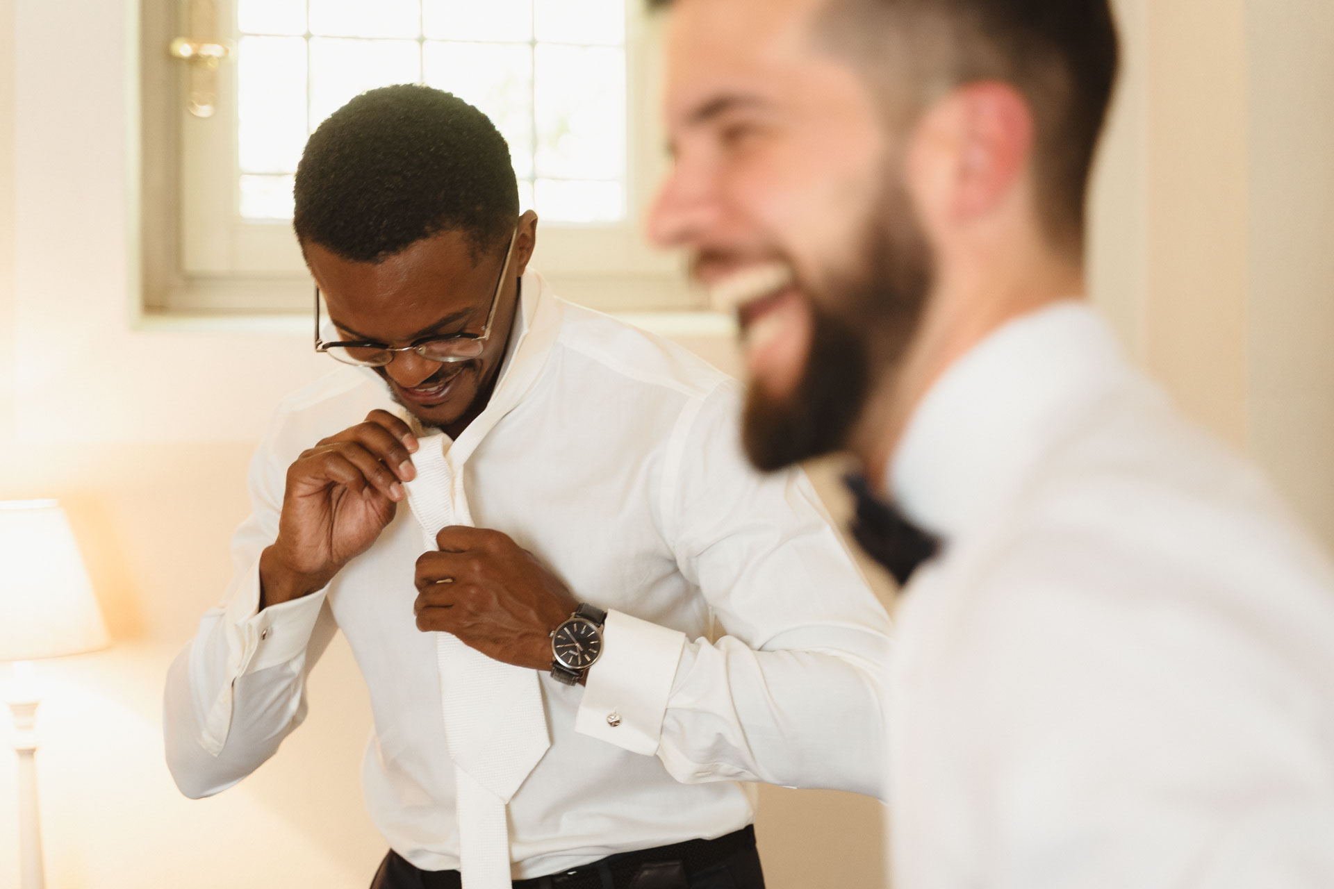 Lo sposo si annoda la cravatta, con un amico che ride in primo piano