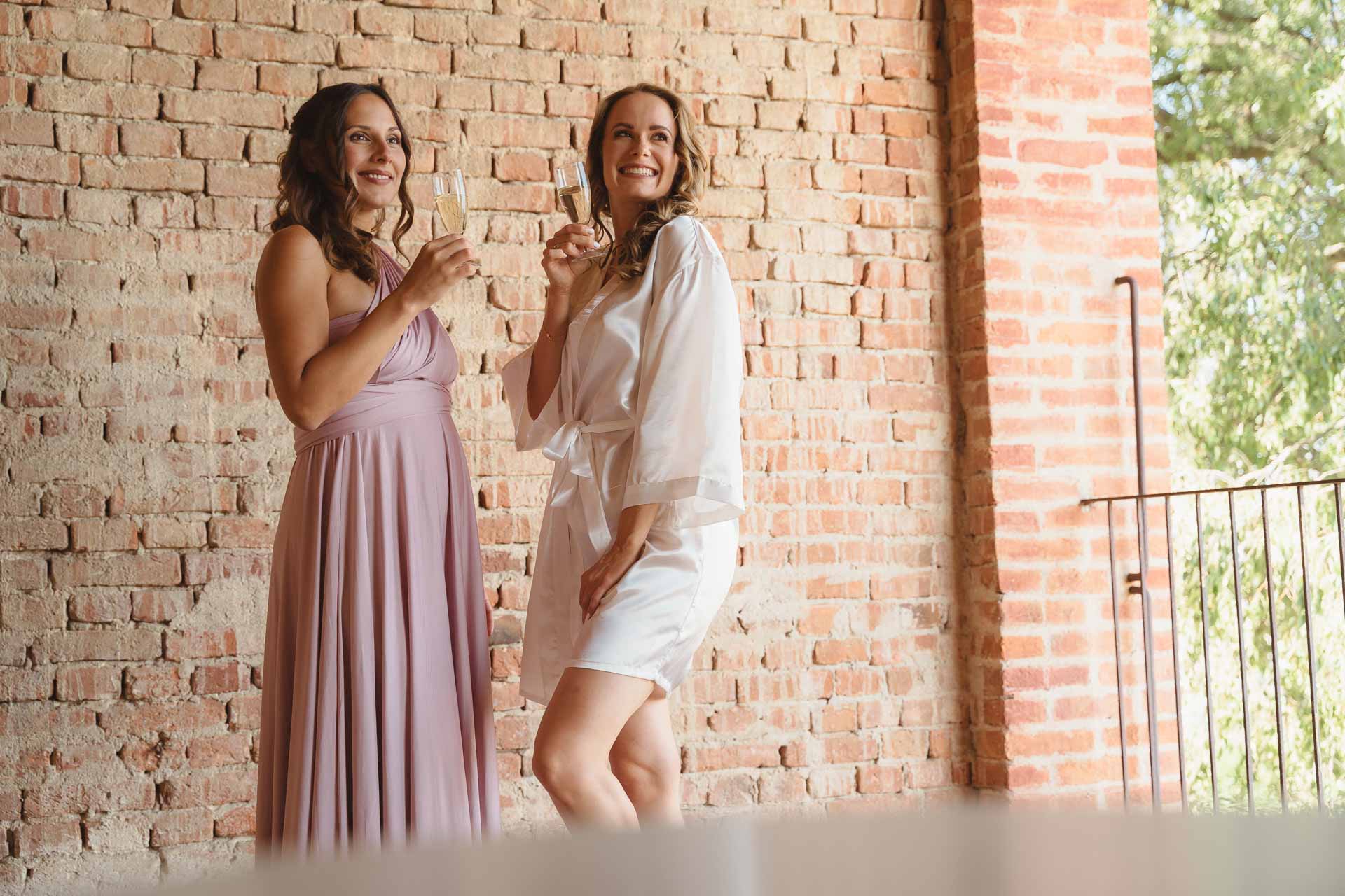 La sposa e un'amica con il calice, contro il muro di mattoni