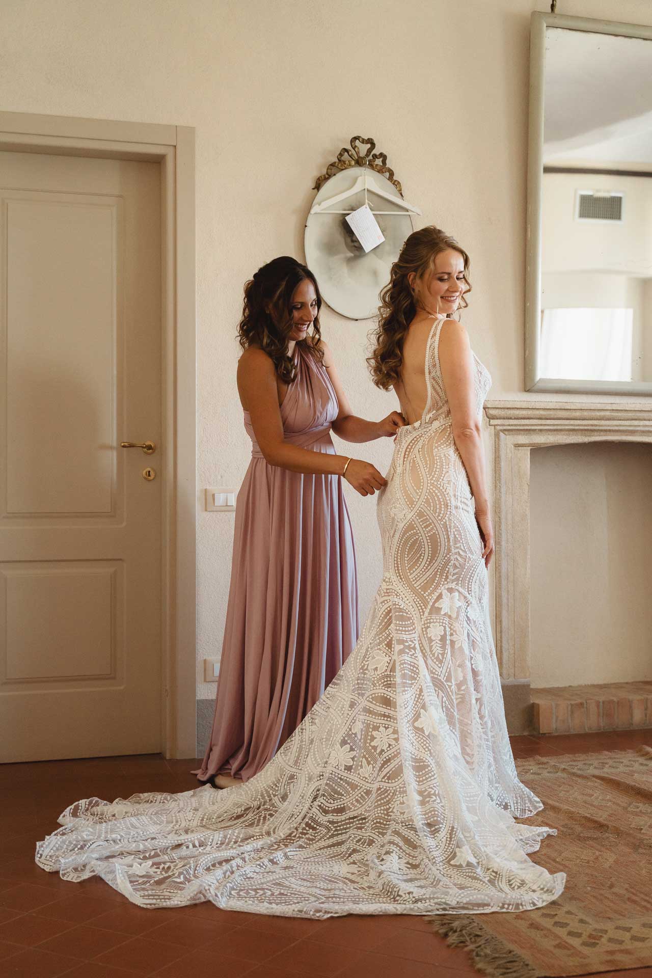 Un'amica allaccia l'abito della sposa, con lo strascico sul pavimento