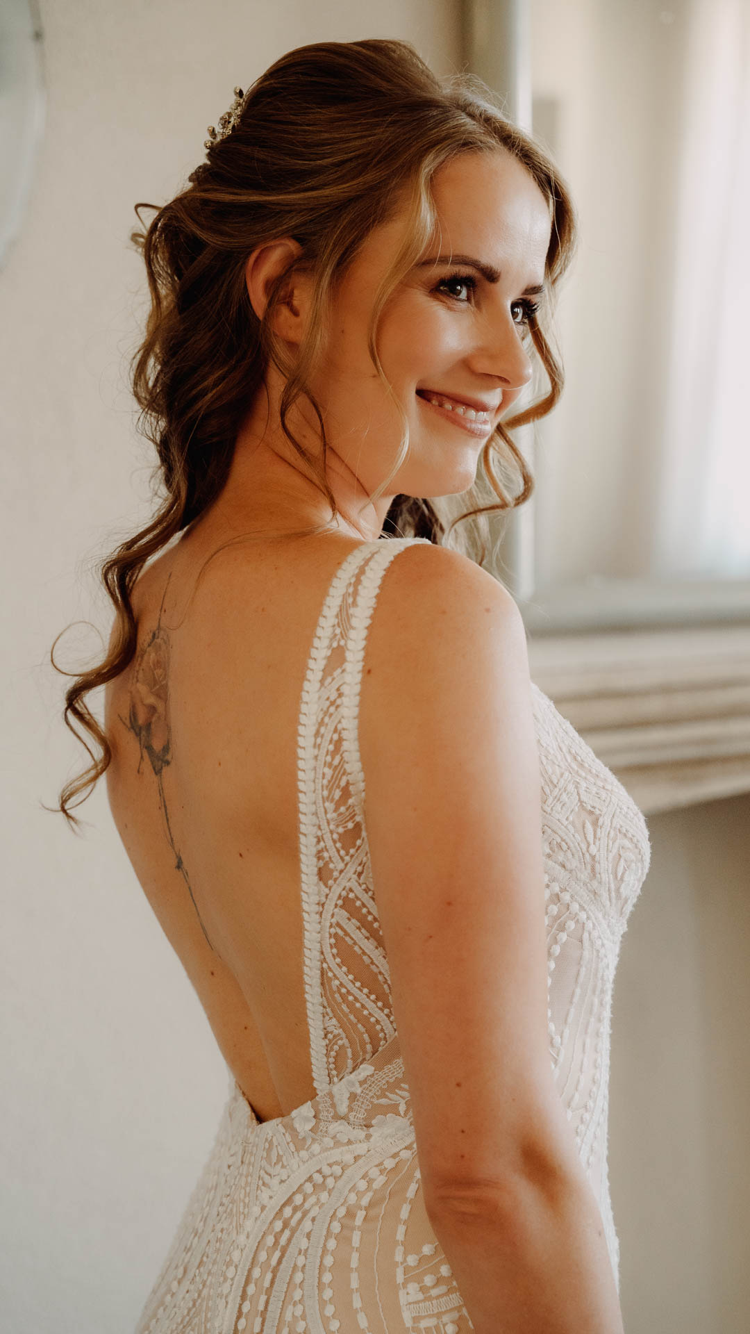 La sposa sorride di spalle, con la schiena scoperta dell'abito