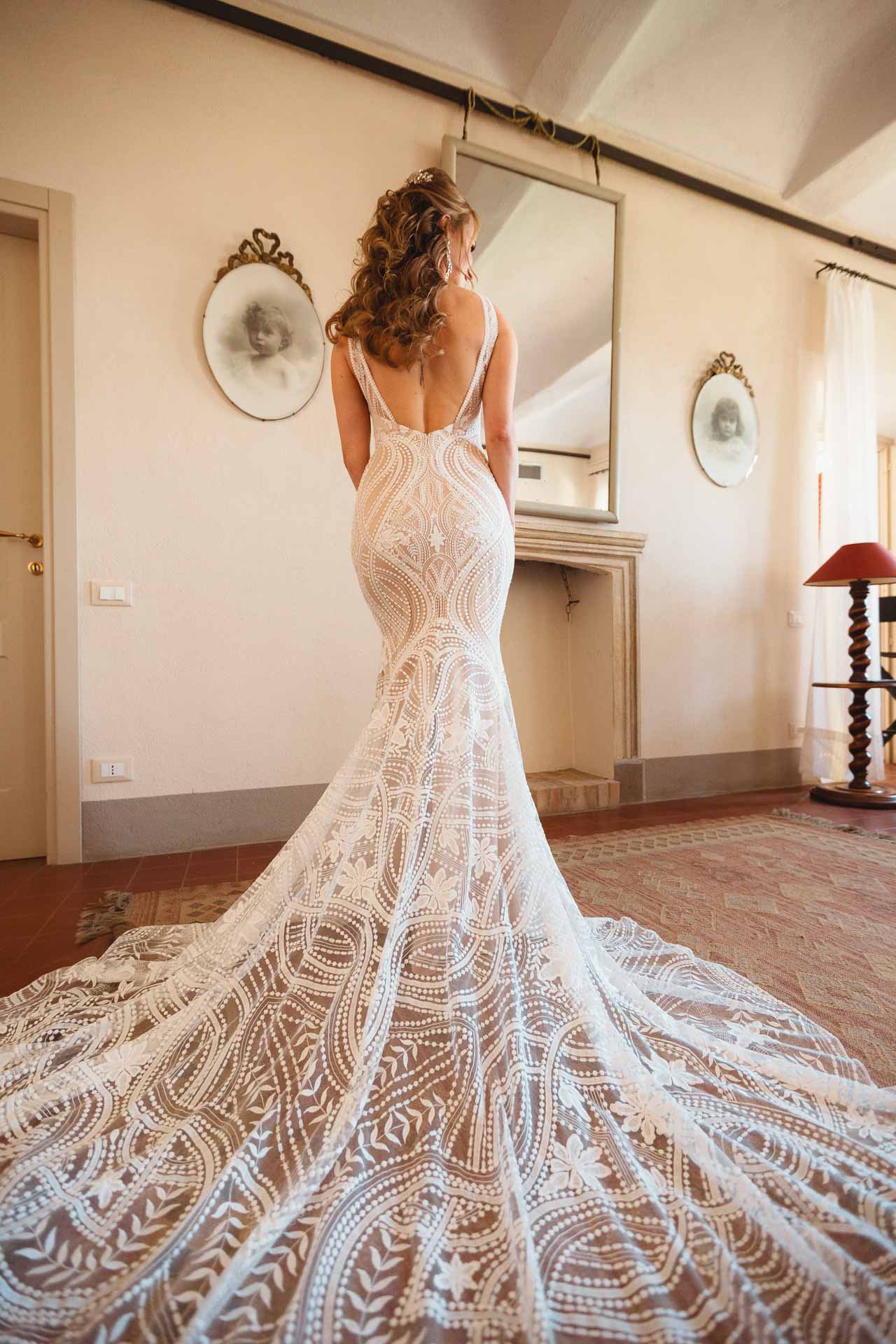 La sposa di spalle, con il lungo strascico di pizzo nella camera