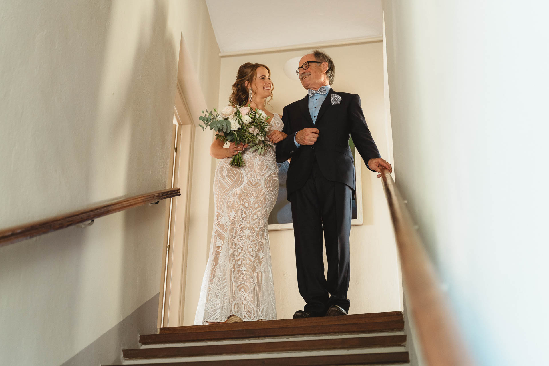 La sposa scende le scale sottobraccio a un signore in abito scuro