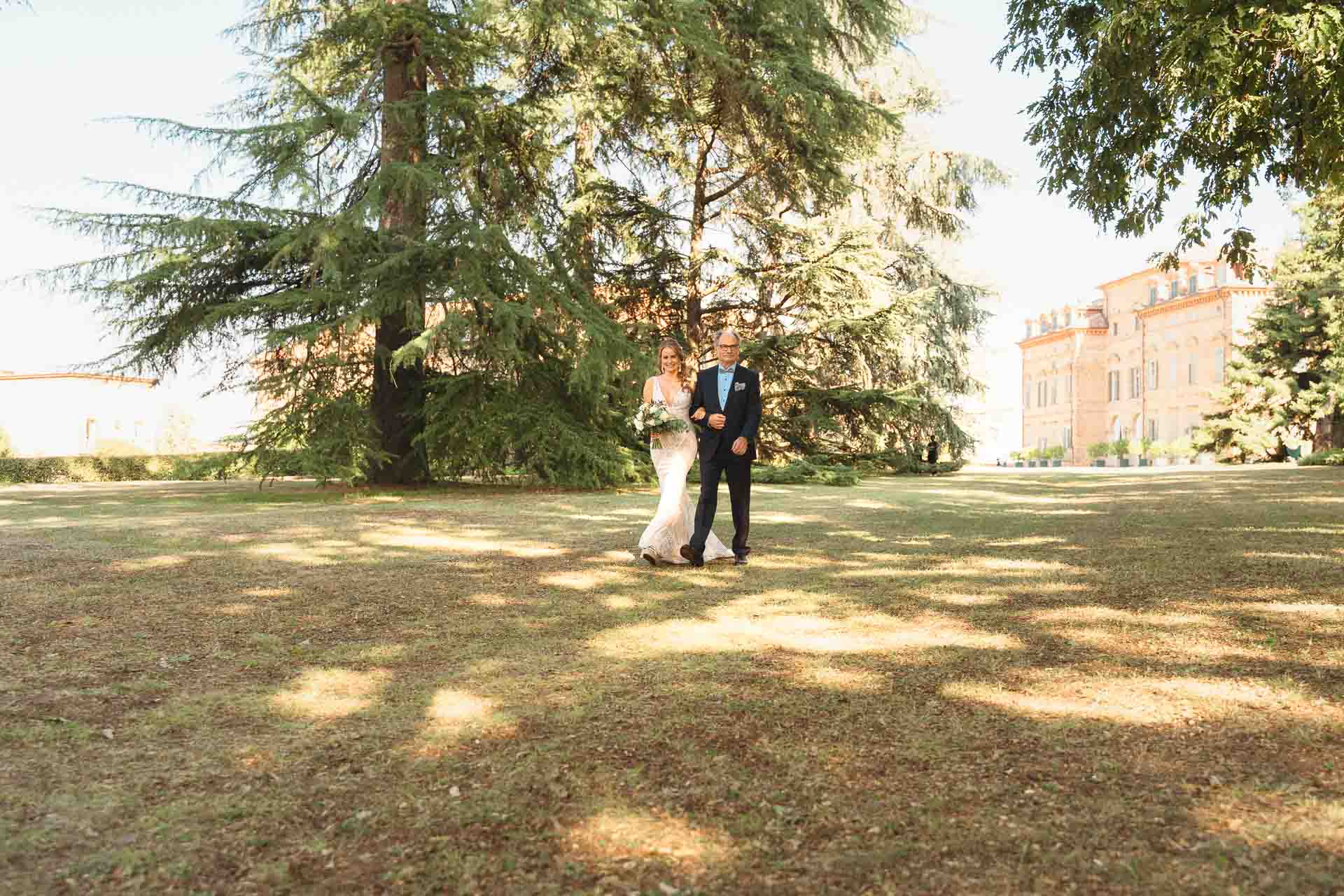 La sposa attraversa il prato verso la cerimonia, tra i cedri