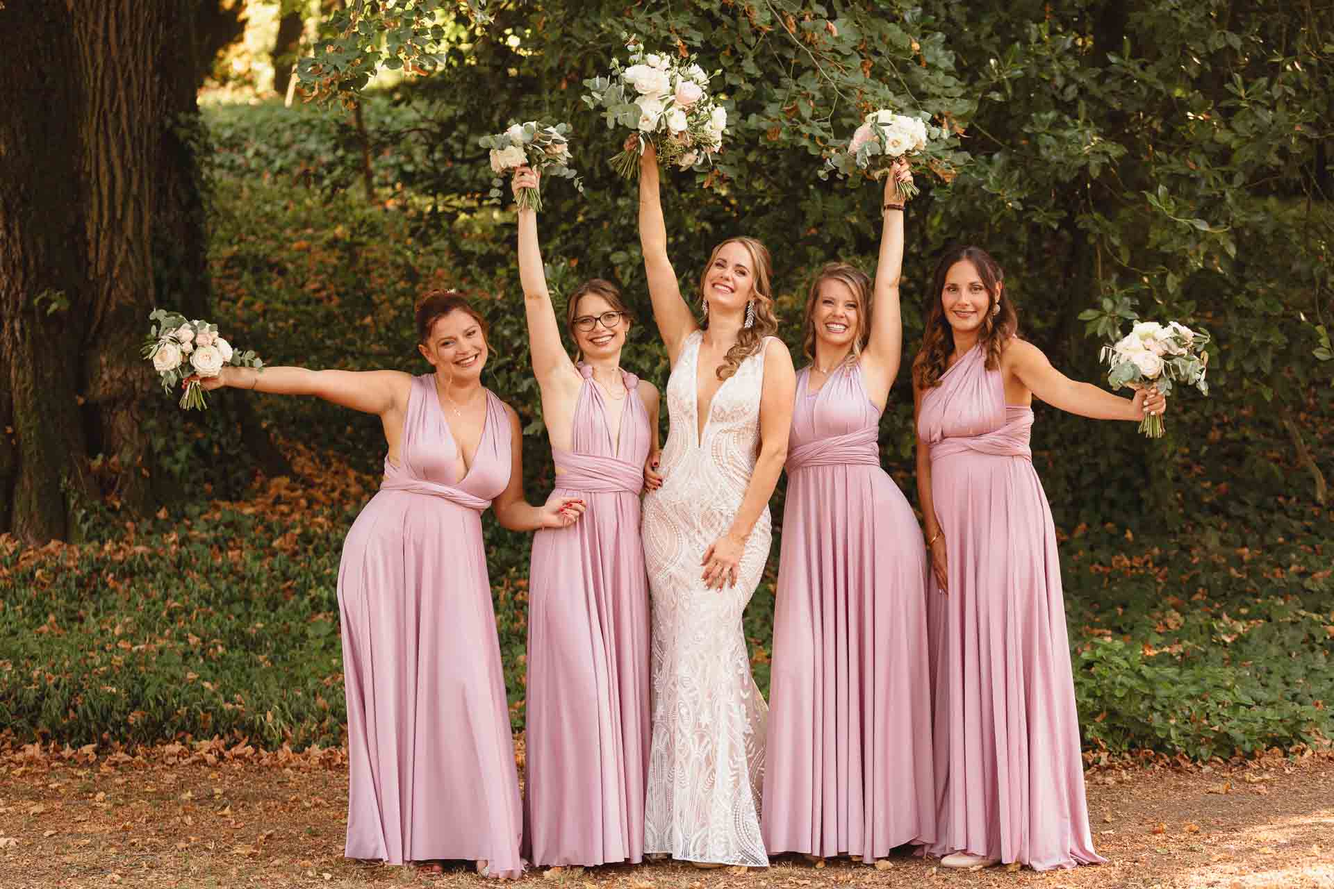 La sposa e le damigelle alzano i bouquet sul prato