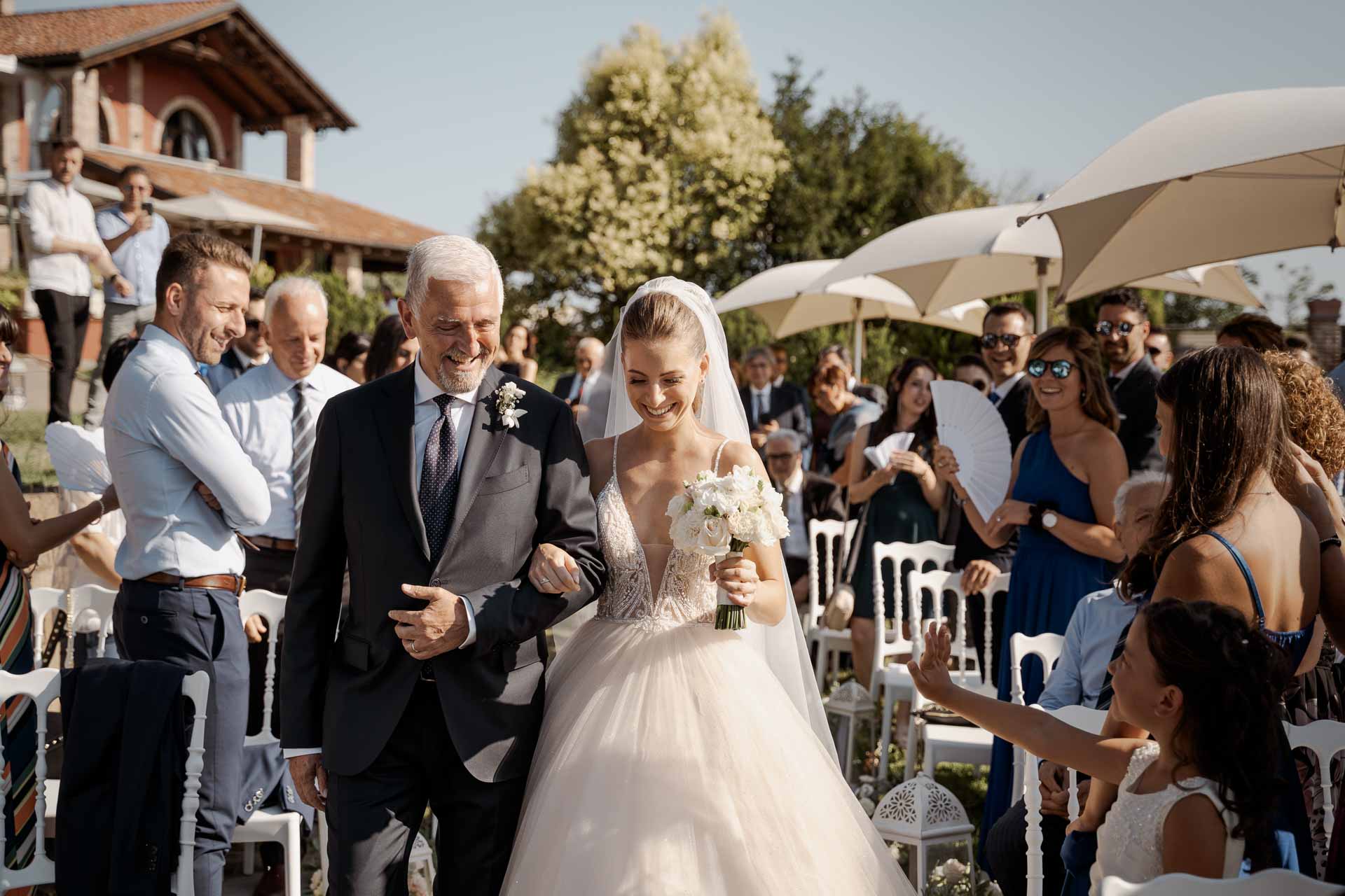 La sposa e il papà percorrono la navata tra gli ombrelloni bianchi