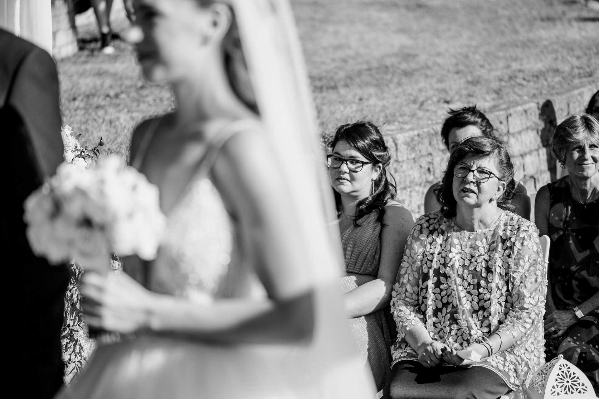 In bianco e nero, il bouquet della sposa e le invitate che ascoltano