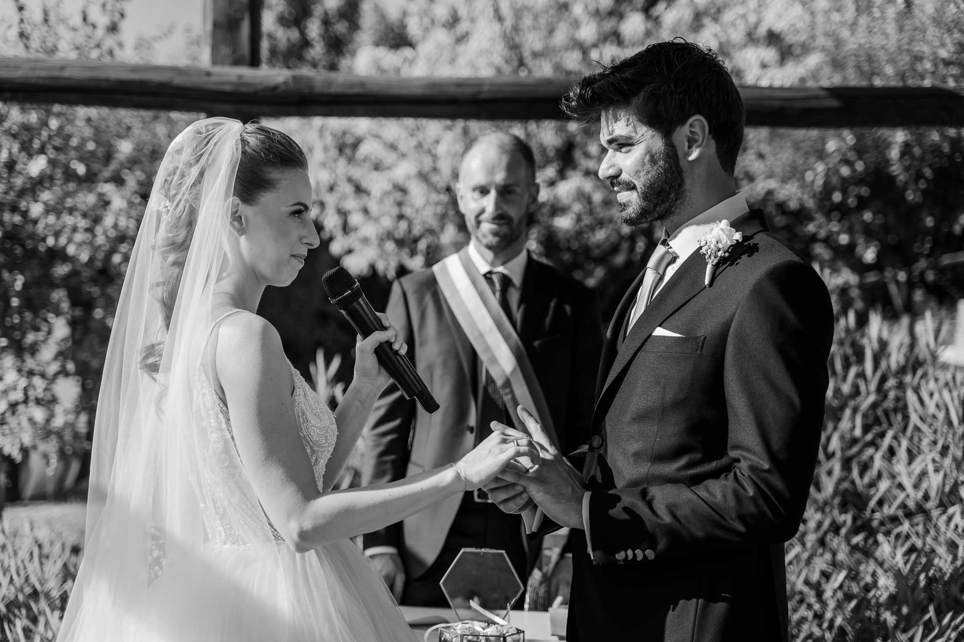 In bianco e nero, la sposa pronuncia le promesse al microfono, la mano in quella dello sposo