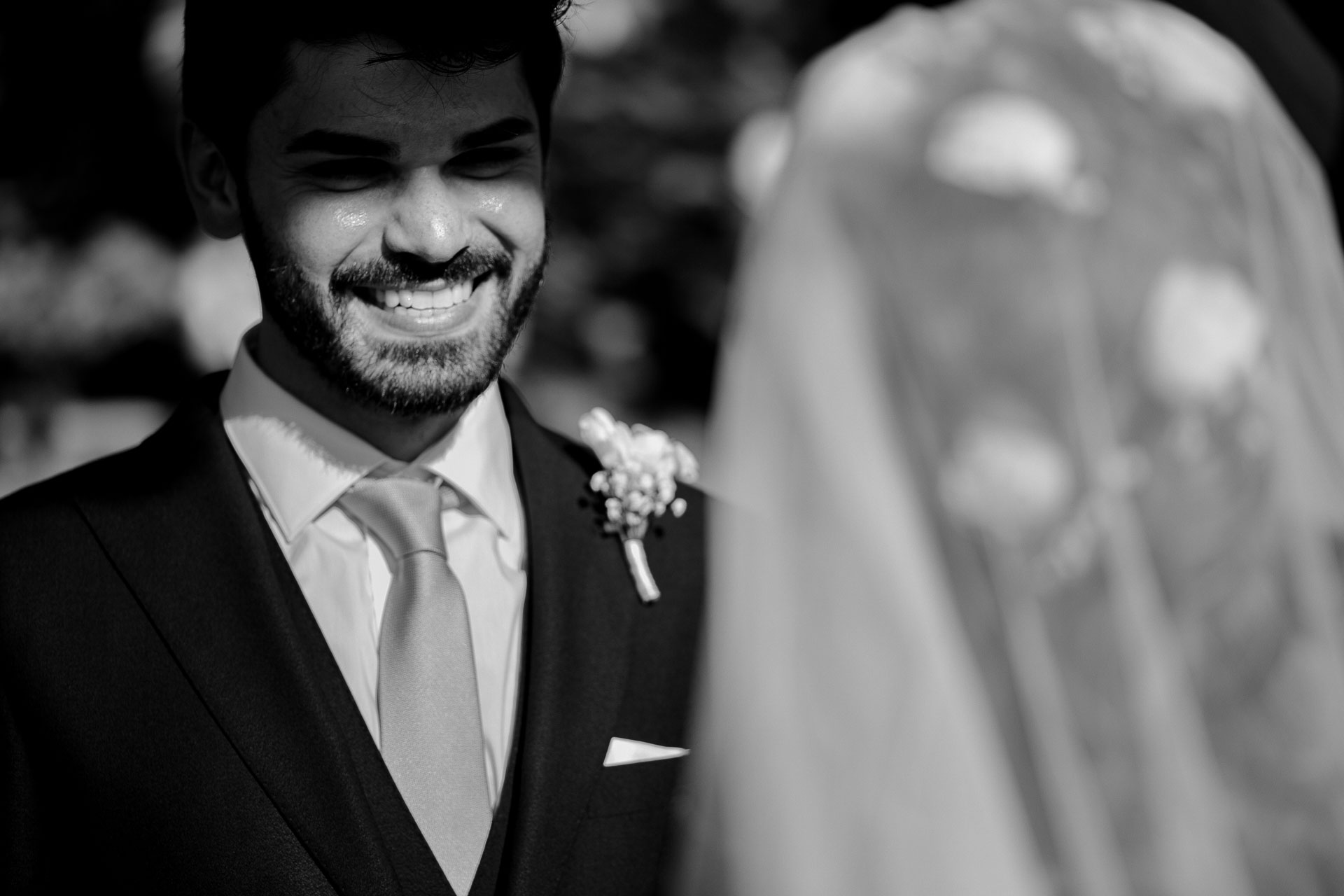 In bianco e nero, il sorriso dello sposo davanti al velo della sposa