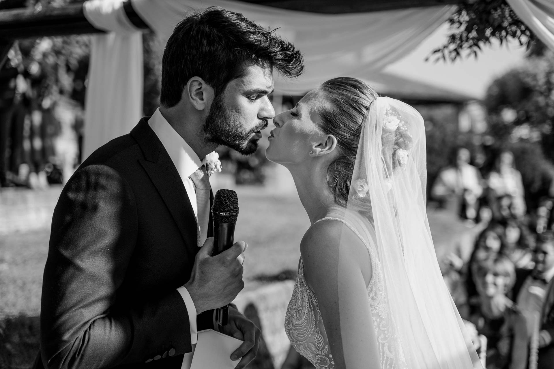 In bianco e nero, il bacio degli sposi con il microfono in mano