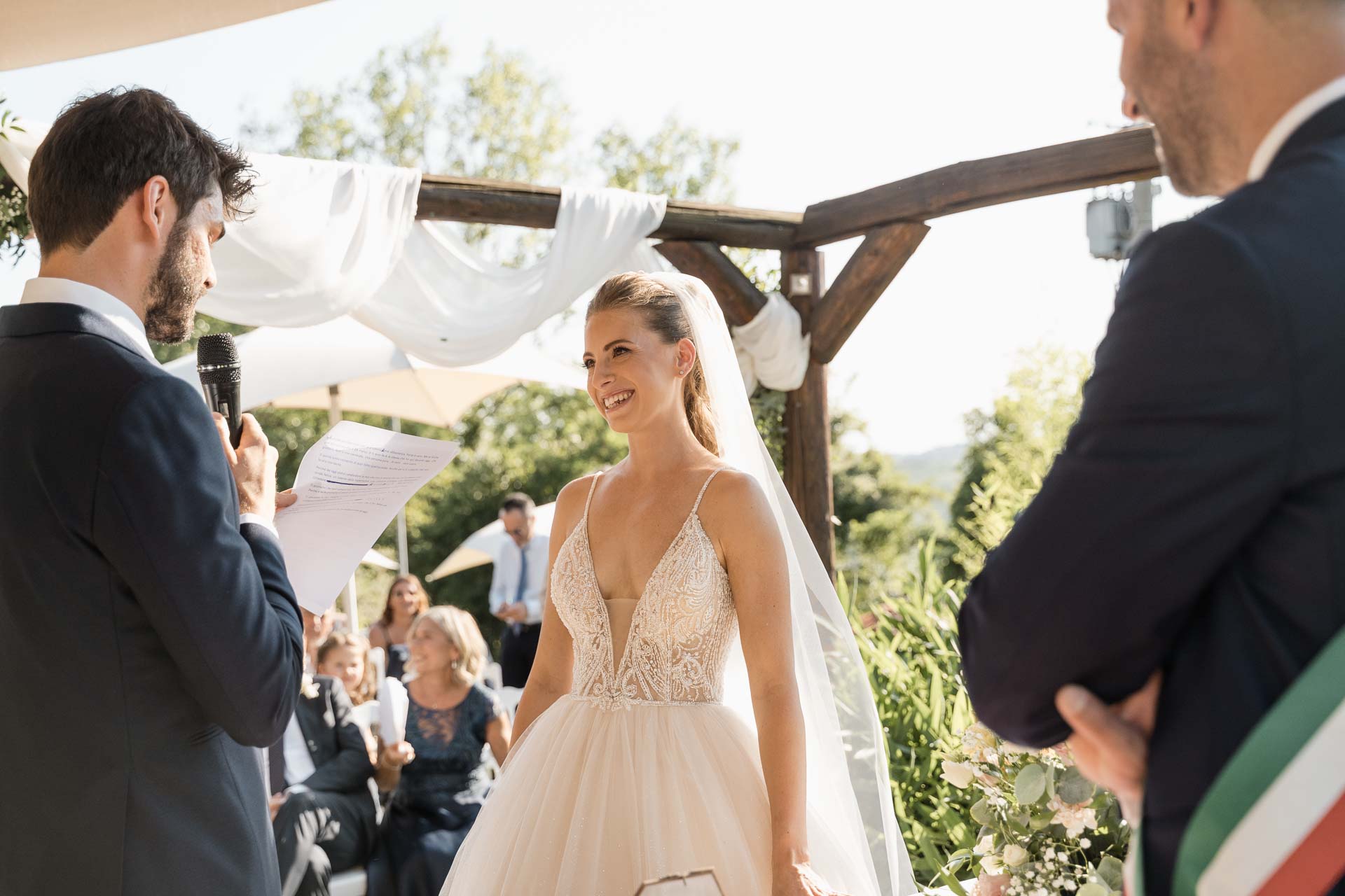 La sposa sorride allo sposo, tra il celebrante e gli invitati