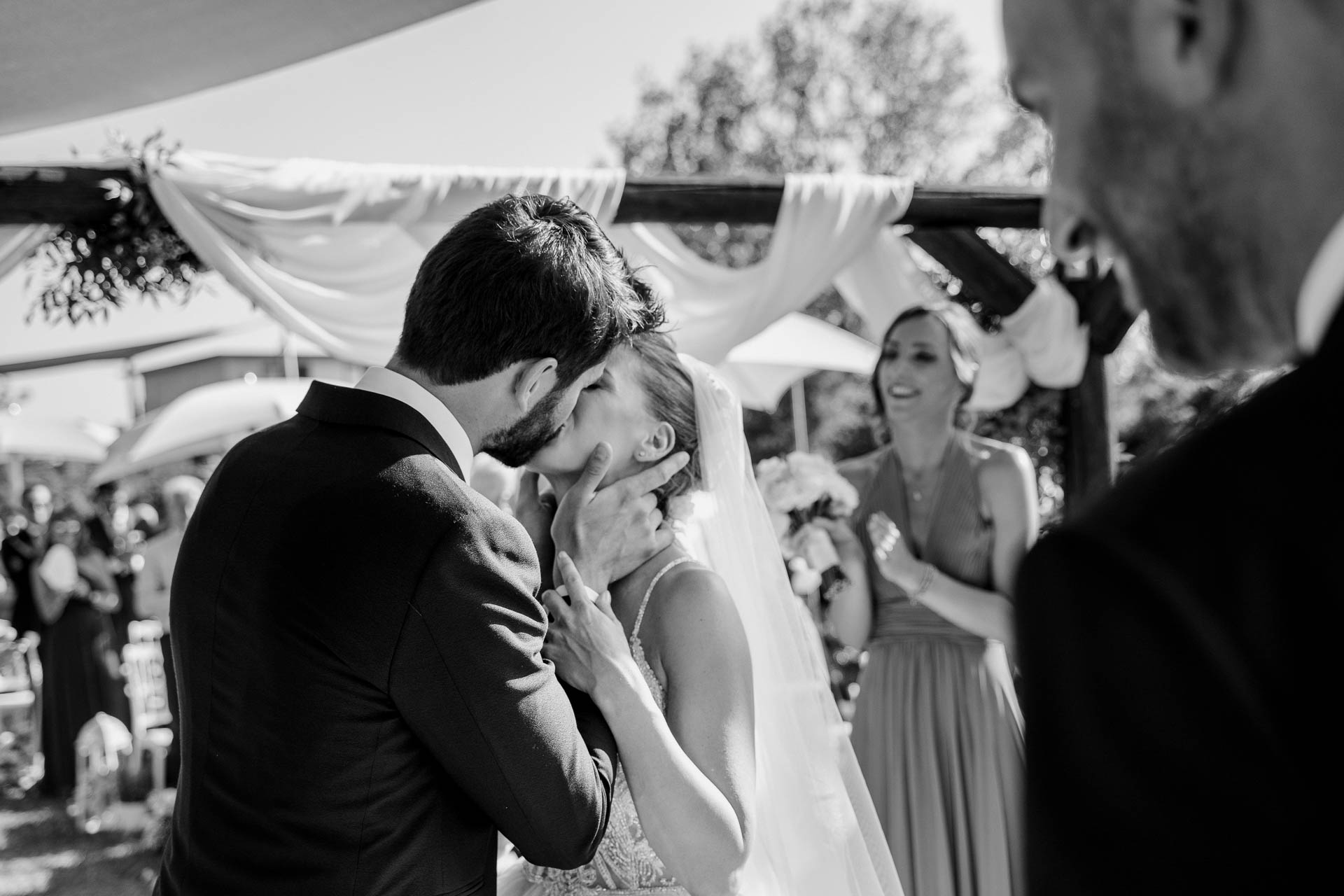 In bianco e nero, la sposa si copre la bocca, emozionata, tra le braccia dello sposo