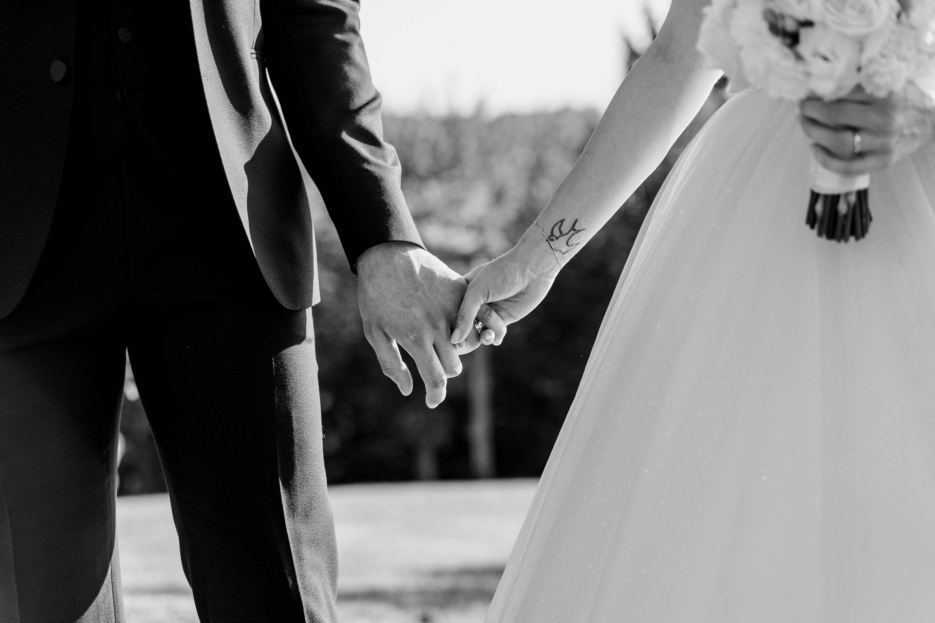 In bianco e nero, le mani degli sposi e il bouquet, nel parco
