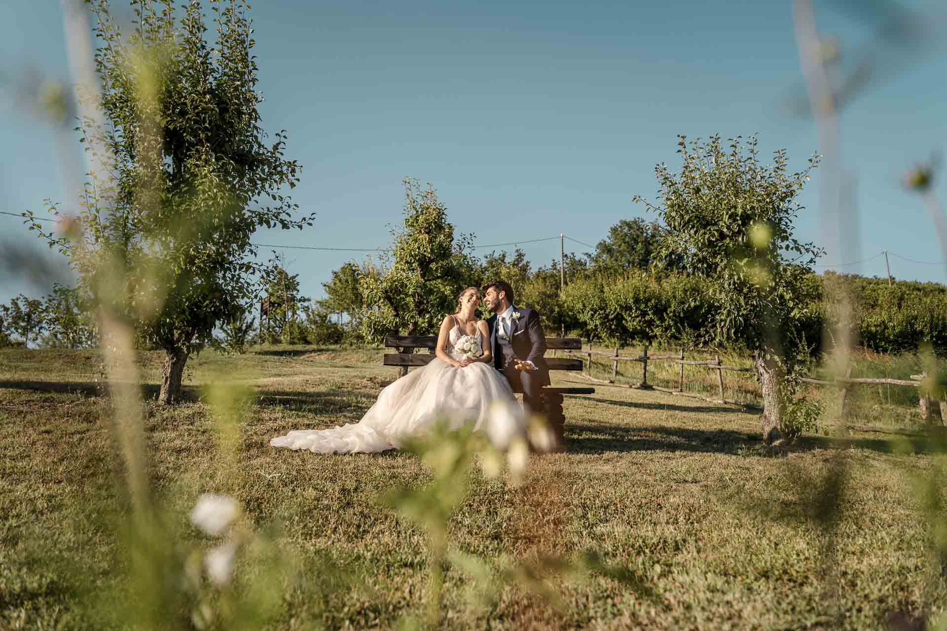 Gli sposi seduti su una panchina tra gli alberi da frutto