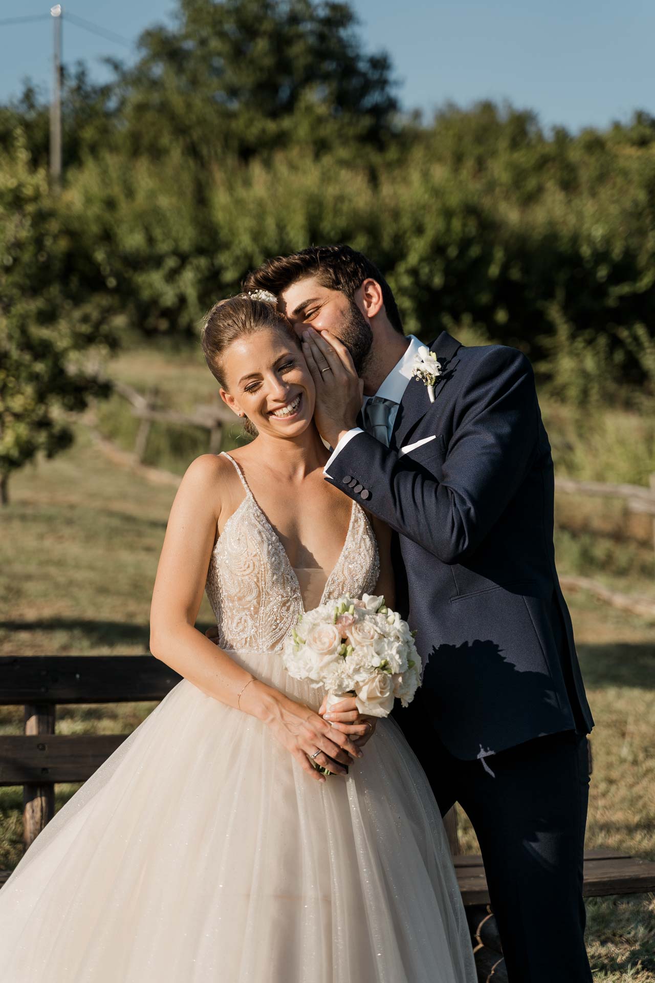 Lo sposo bacia la sposa sulla guancia, nel sole del pomeriggio