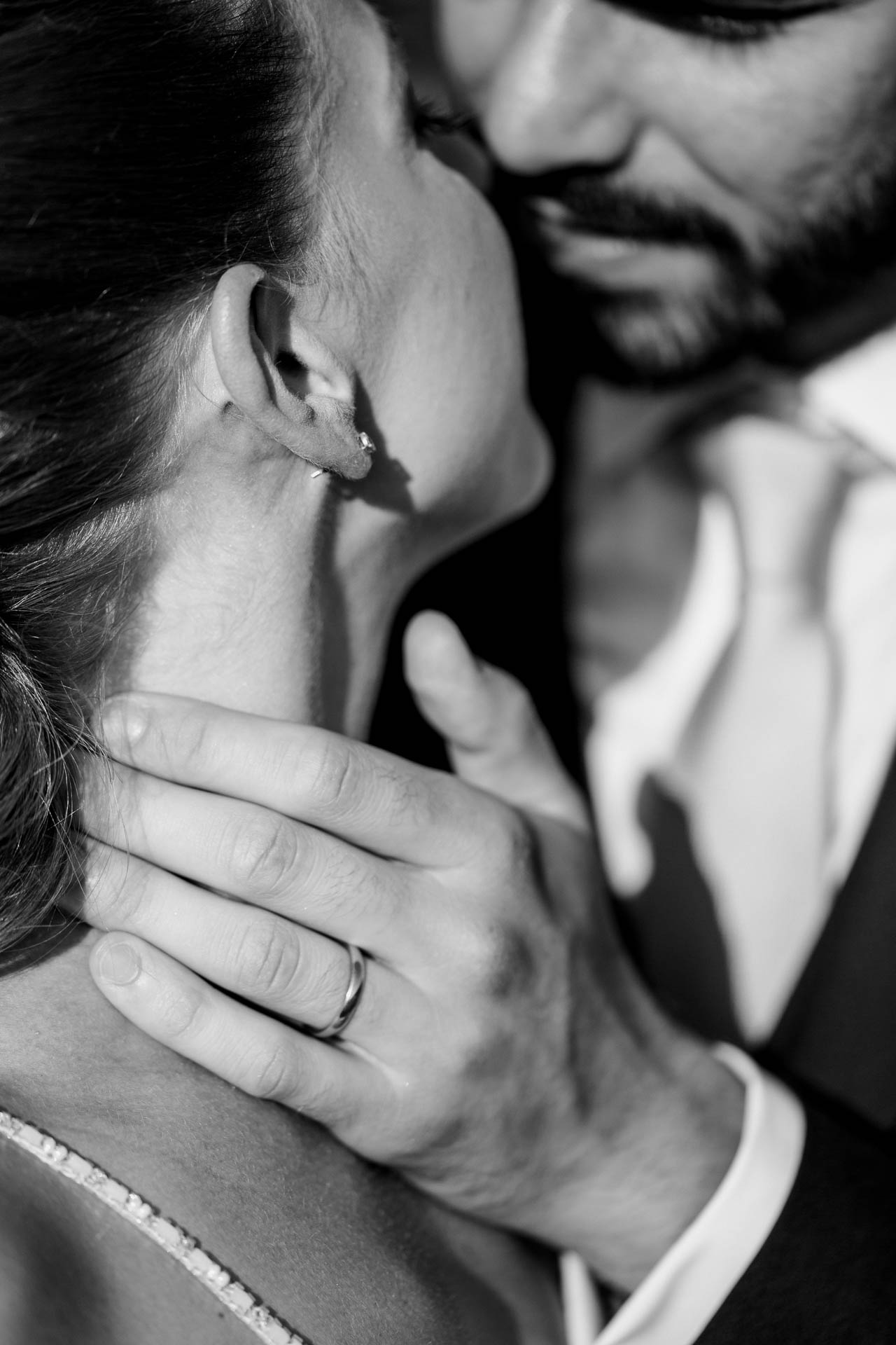 In bianco e nero, la mano dello sposo con la fede sul collo della sposa