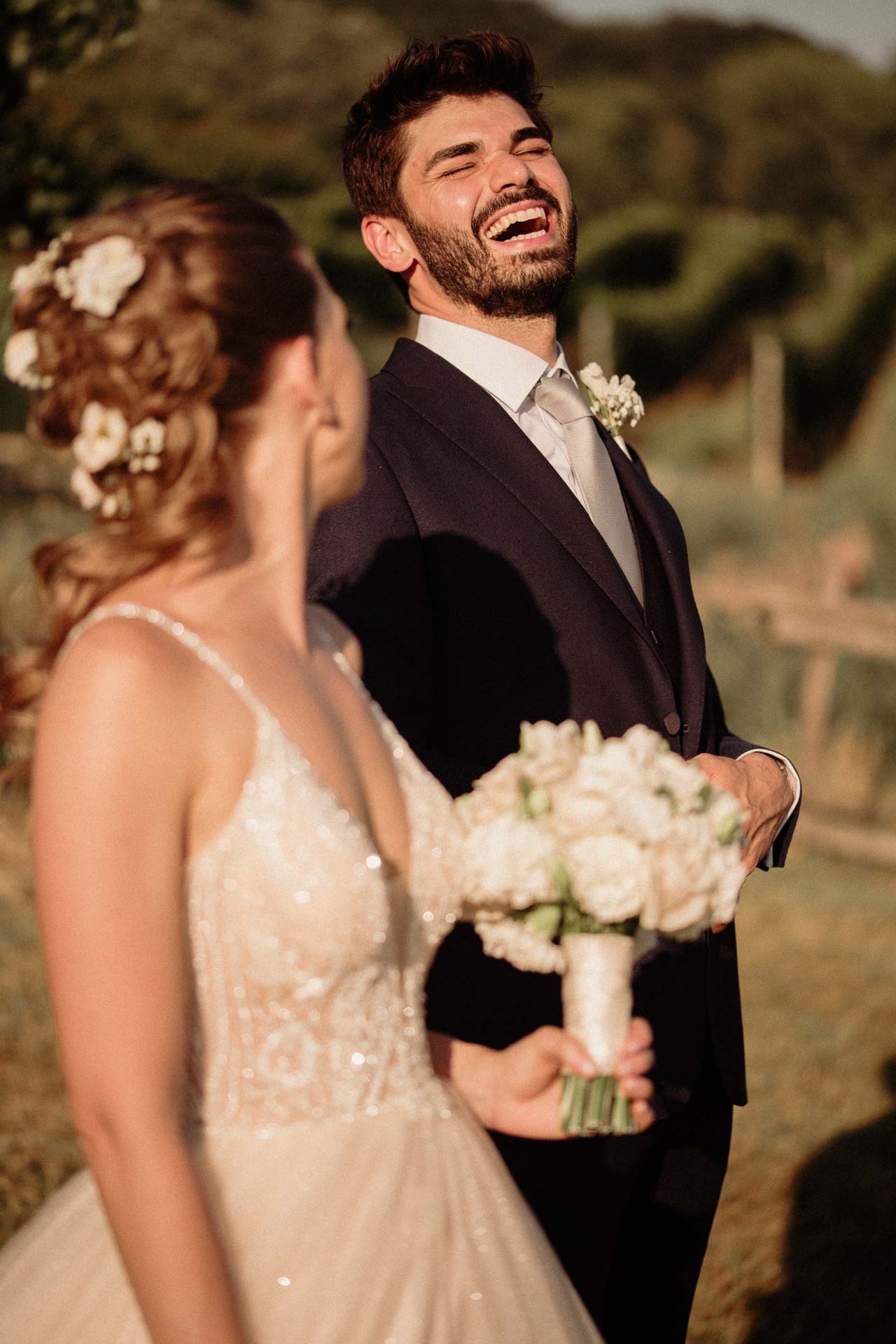 Lo sposo scoppia a ridere accanto alla sposa, nella luce calda