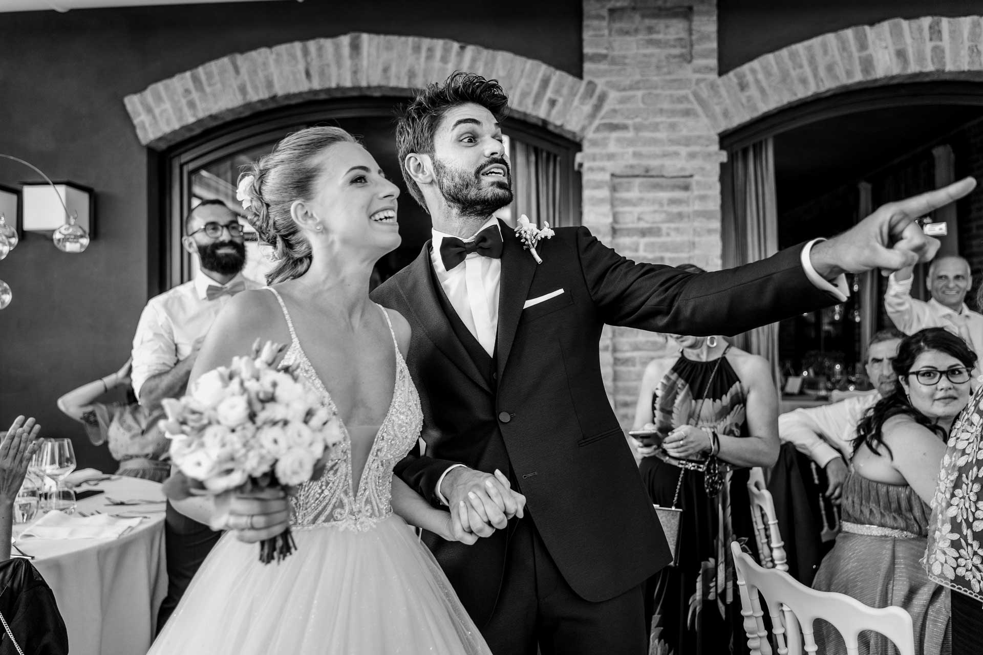 In bianco e nero, gli sposi entrano ridendo e lo sposo indica qualcuno tra gli invitati