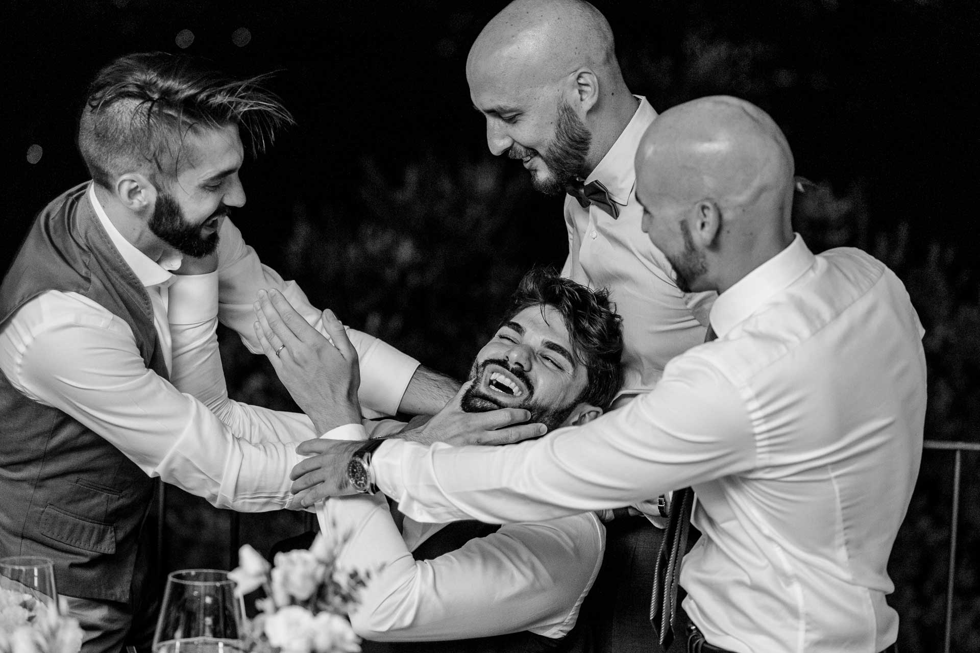 In bianco e nero, gli amici stringono lo sposo in un abbraccio, ridendo