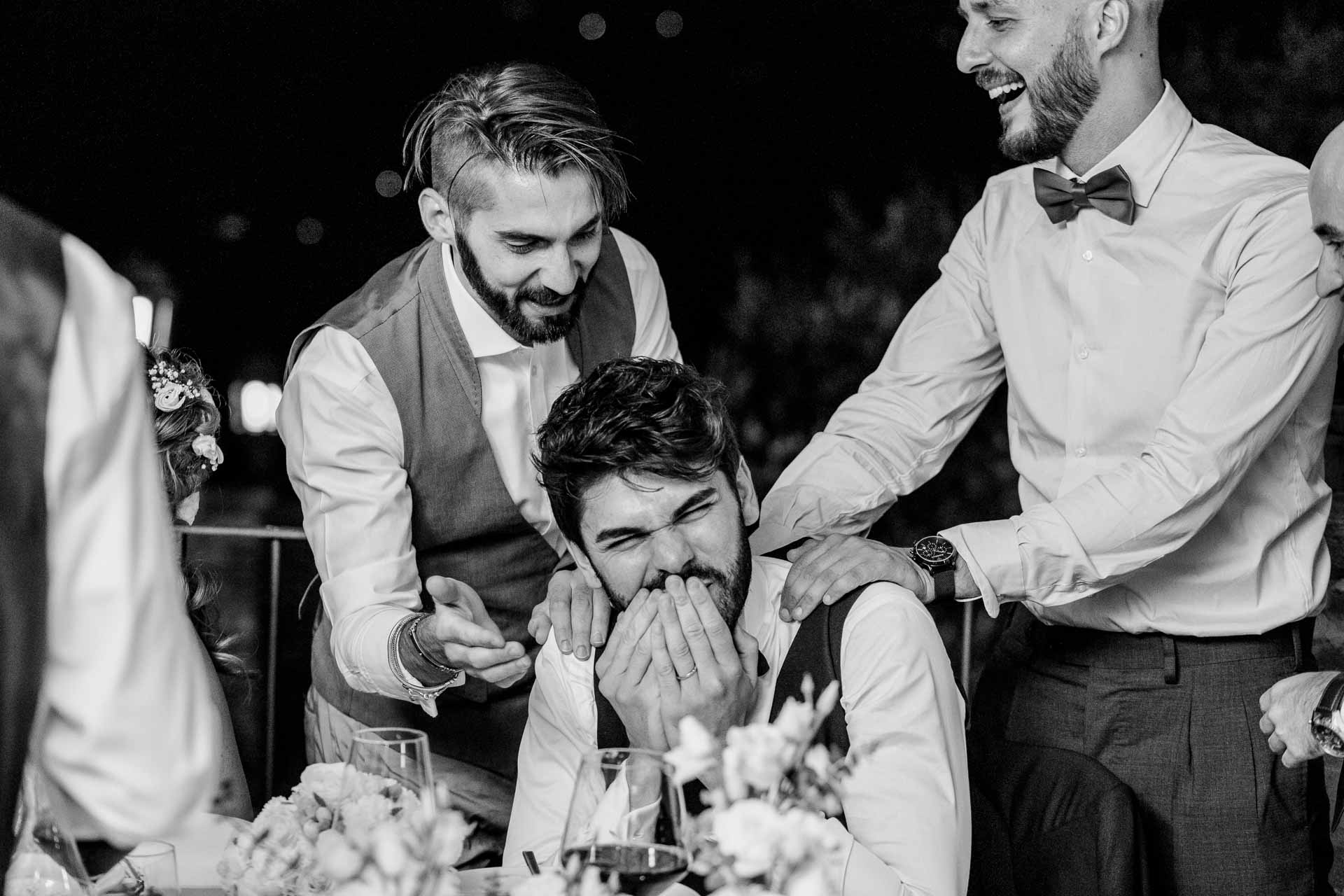 In bianco e nero, lo sposo ride coprendosi il viso, tra gli amici