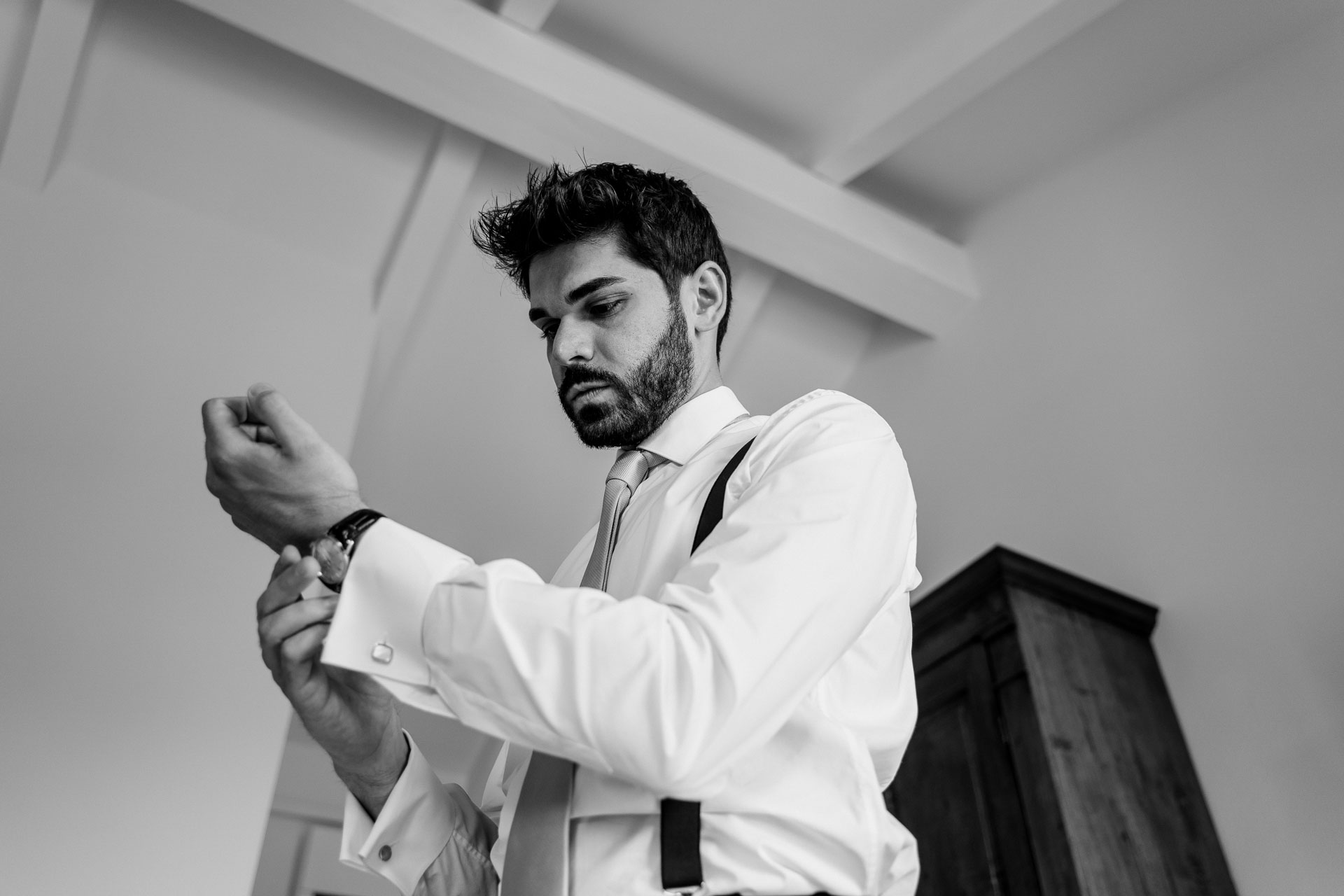 In bianco e nero, lo sposo si allaccia l'orologio sotto le travi del soffitto