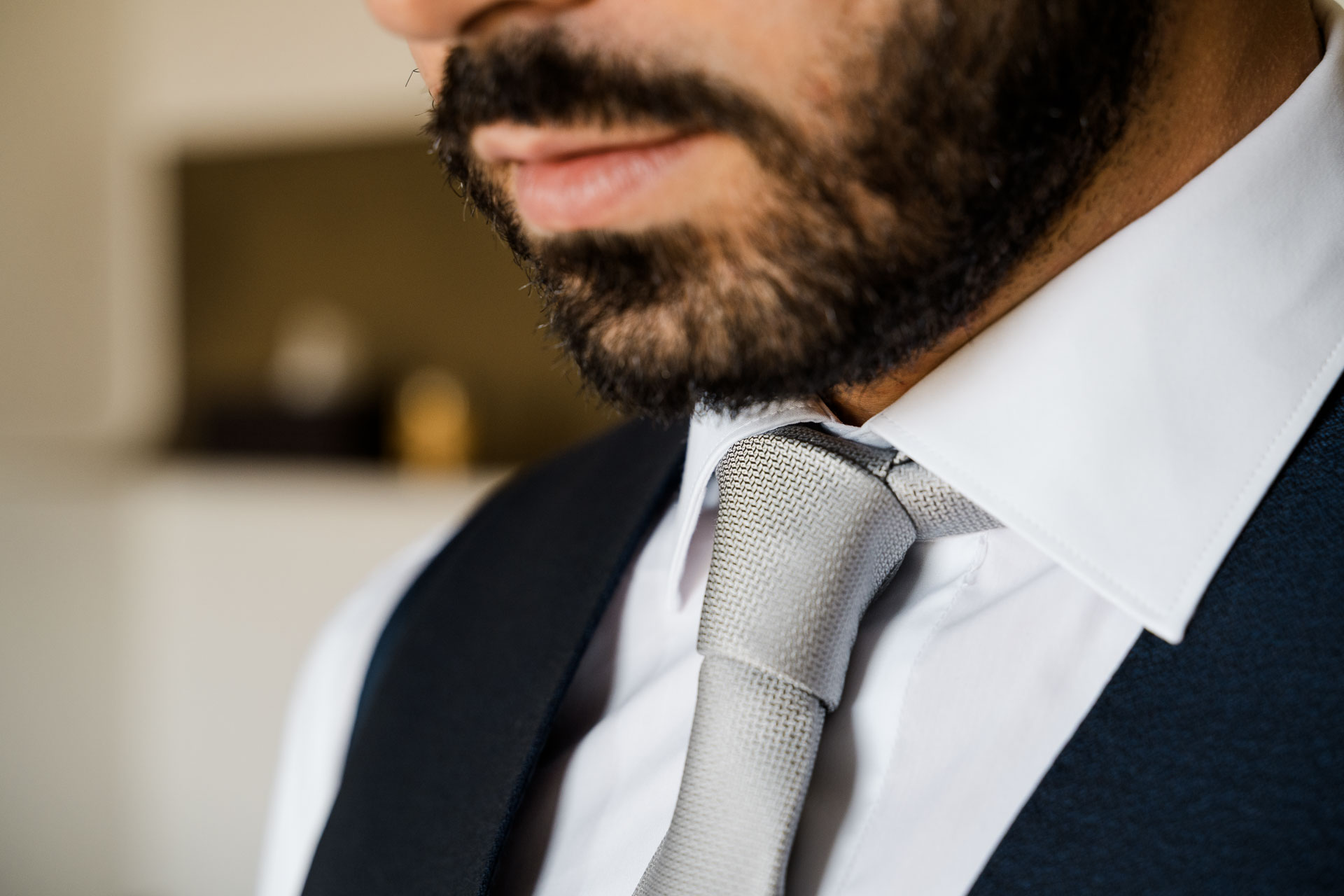 La barba, il colletto bianco e la cravatta grigia sul gilet blu