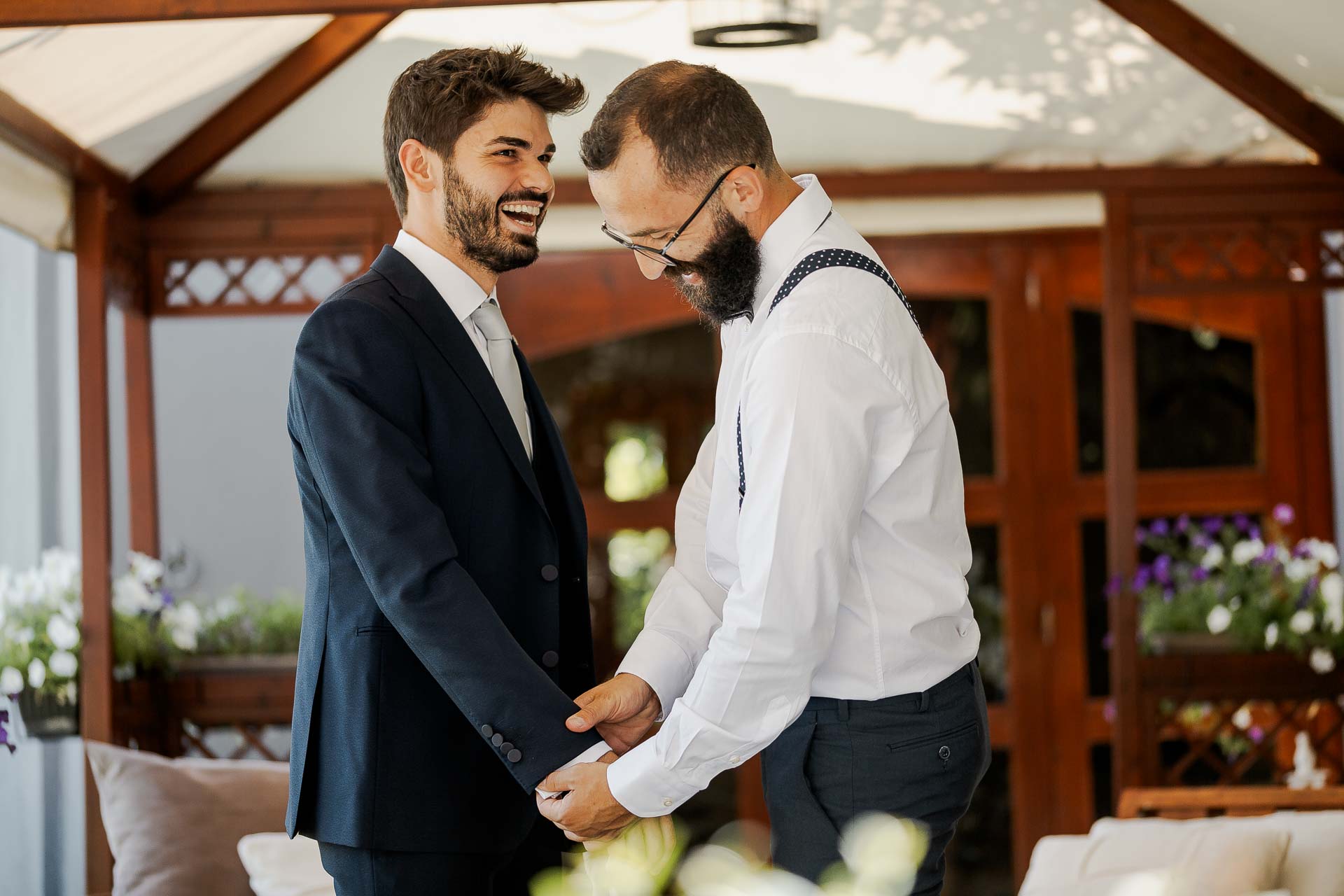 Lo sposo e l'amico ridono sotto il gazebo di legno, tra i fiori