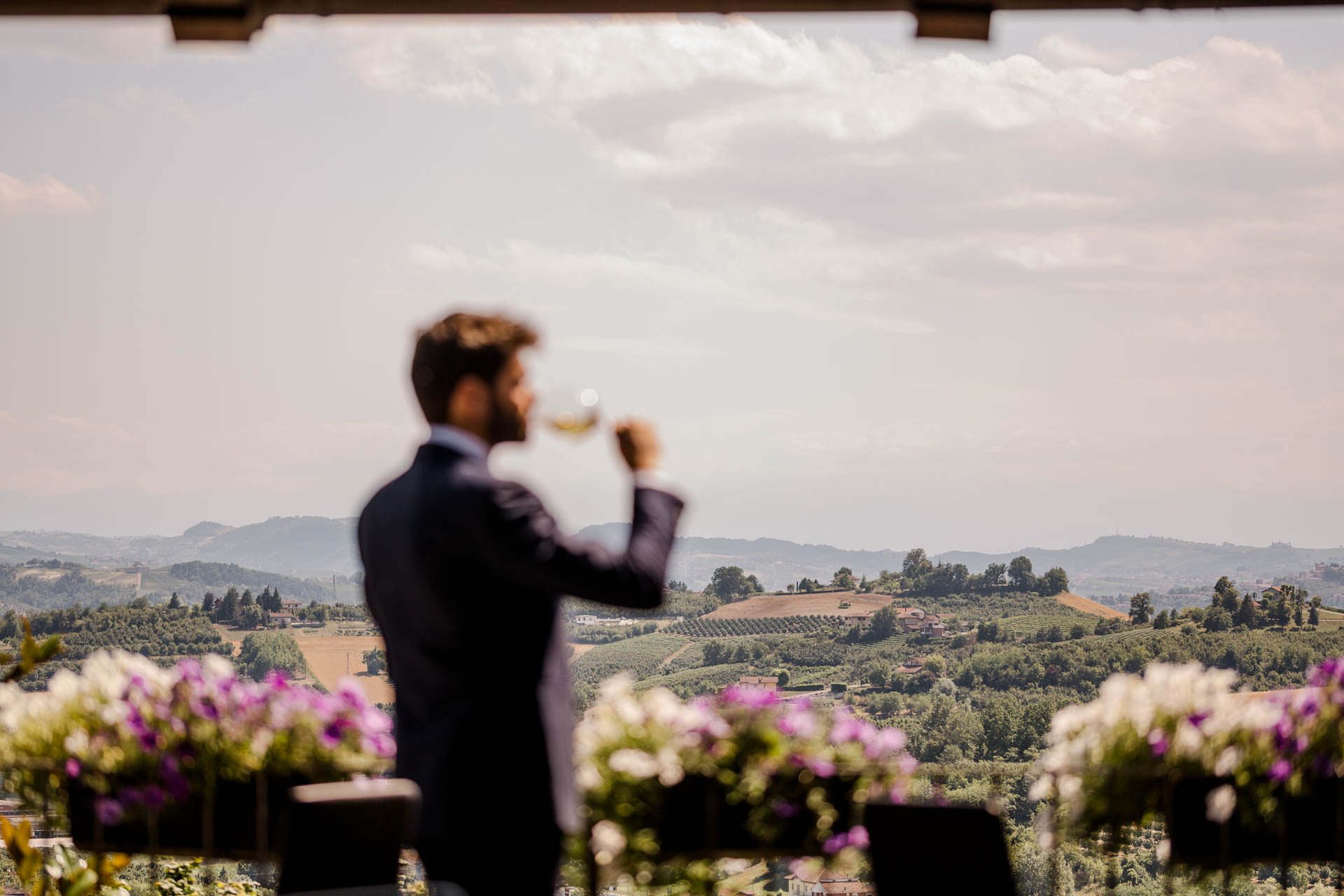 Lo sposo beve un calice di vino davanti alle colline, tra le petunie