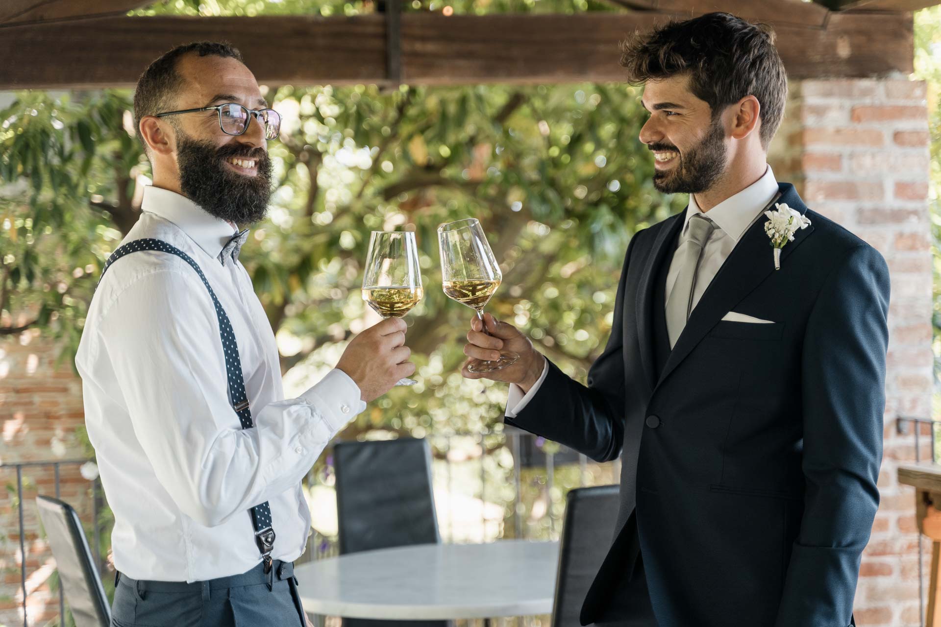 Lo sposo e l'amico brindano con il vino bianco sotto il portico