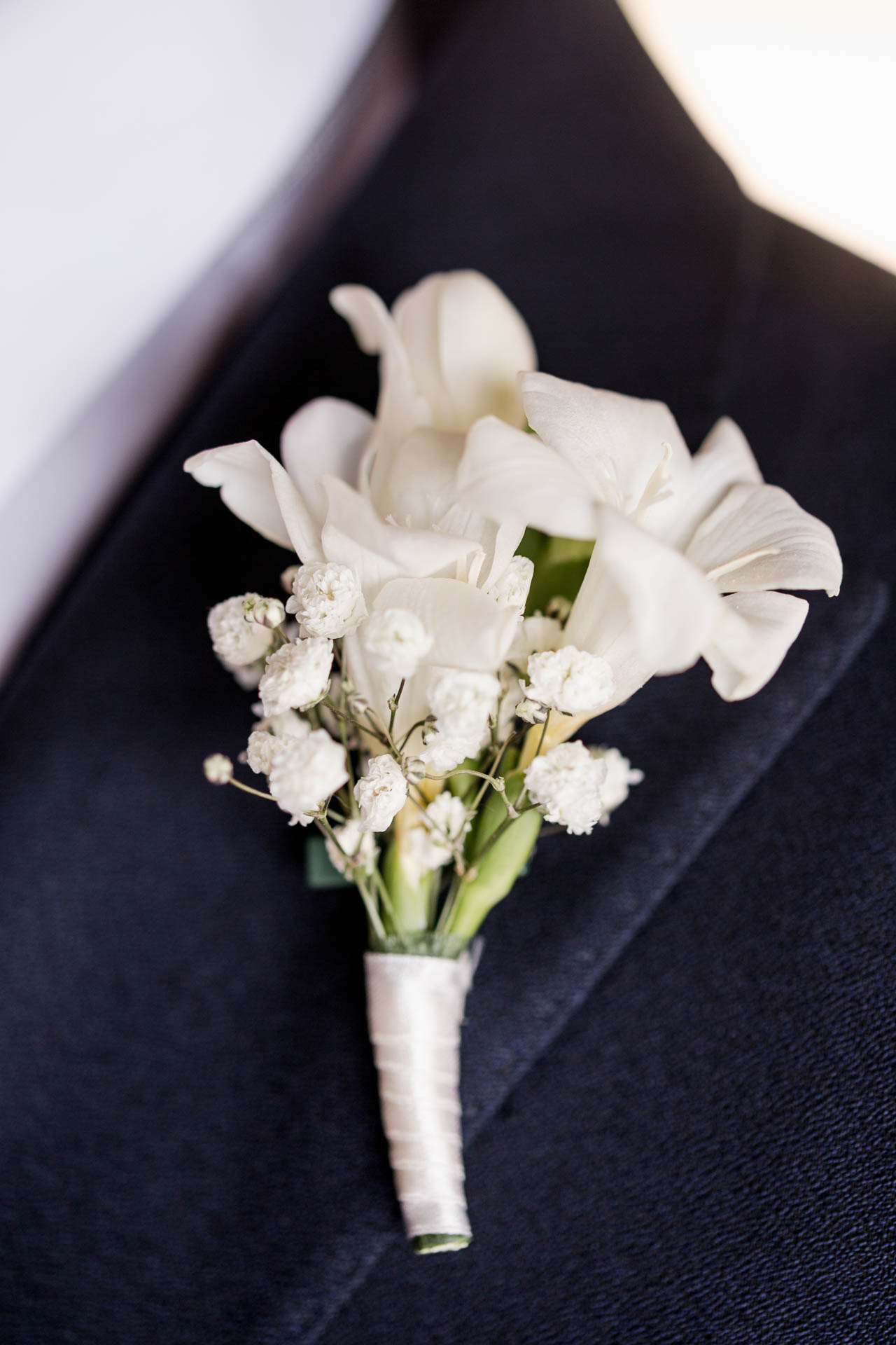 Il fiore all'occhiello bianco, con il nastro di raso, sulla giacca blu
