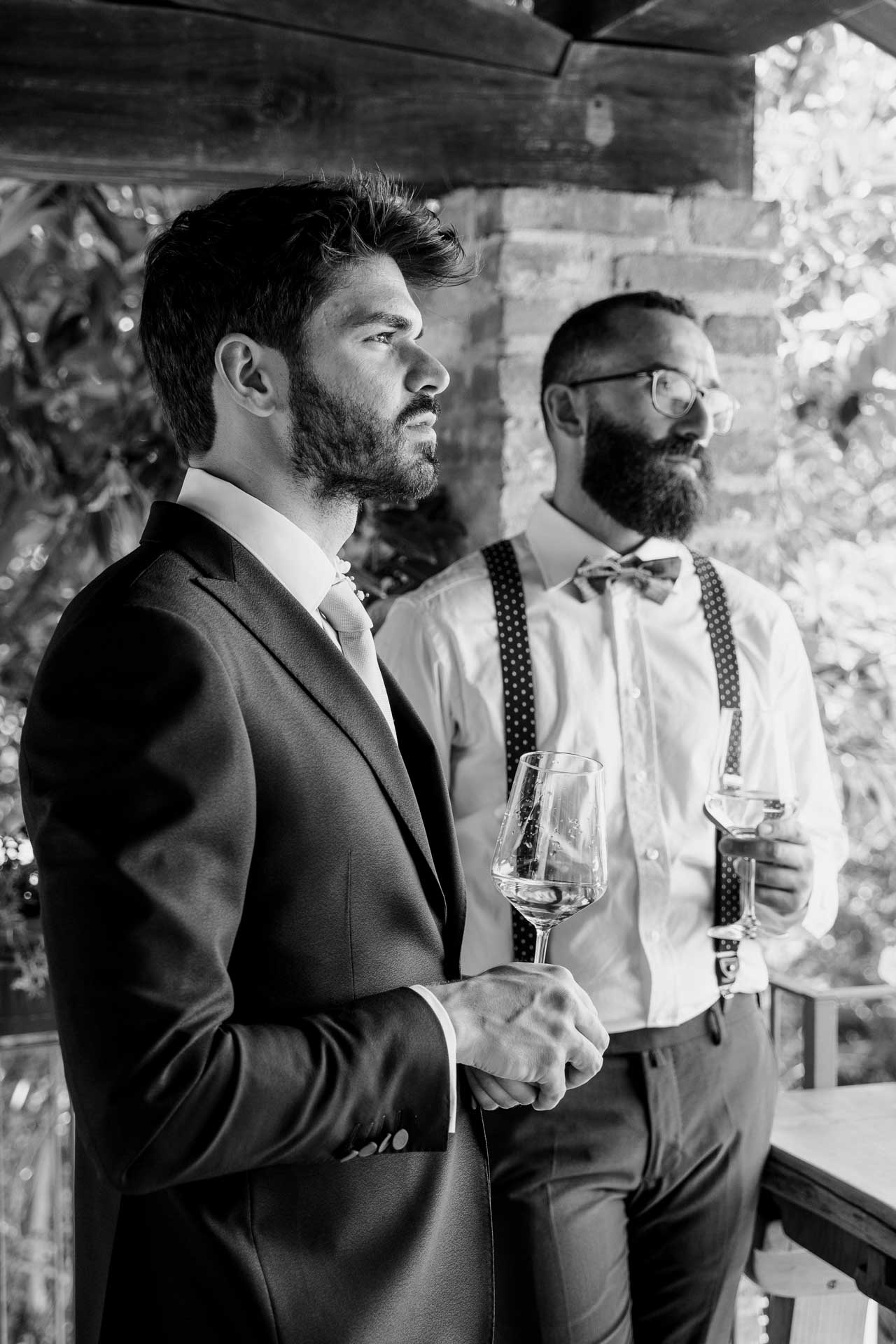 In bianco e nero, lo sposo e l'amico con il calice in mano, sotto il portico