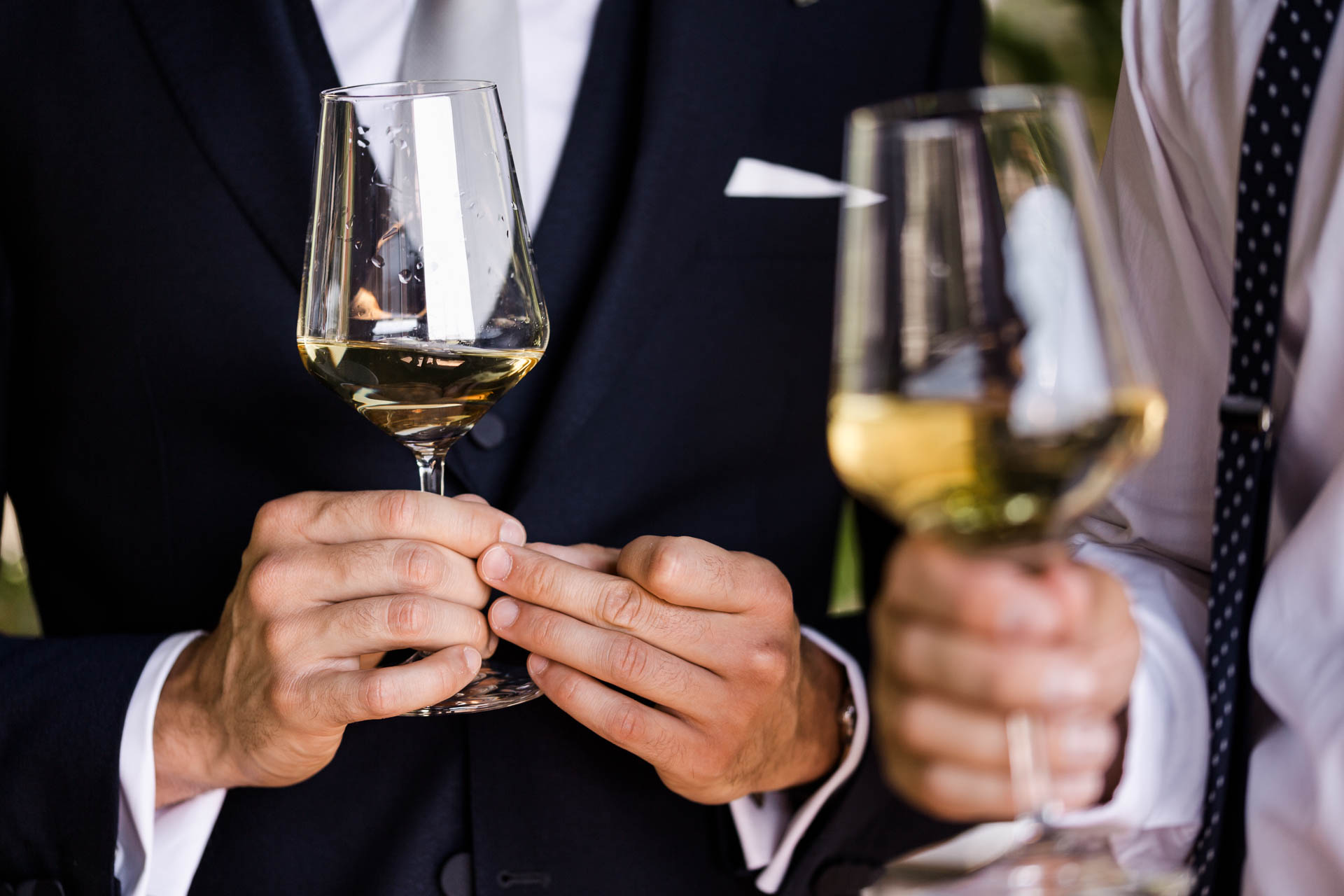 Le mani dello sposo e dell'amico con i calici di vino bianco