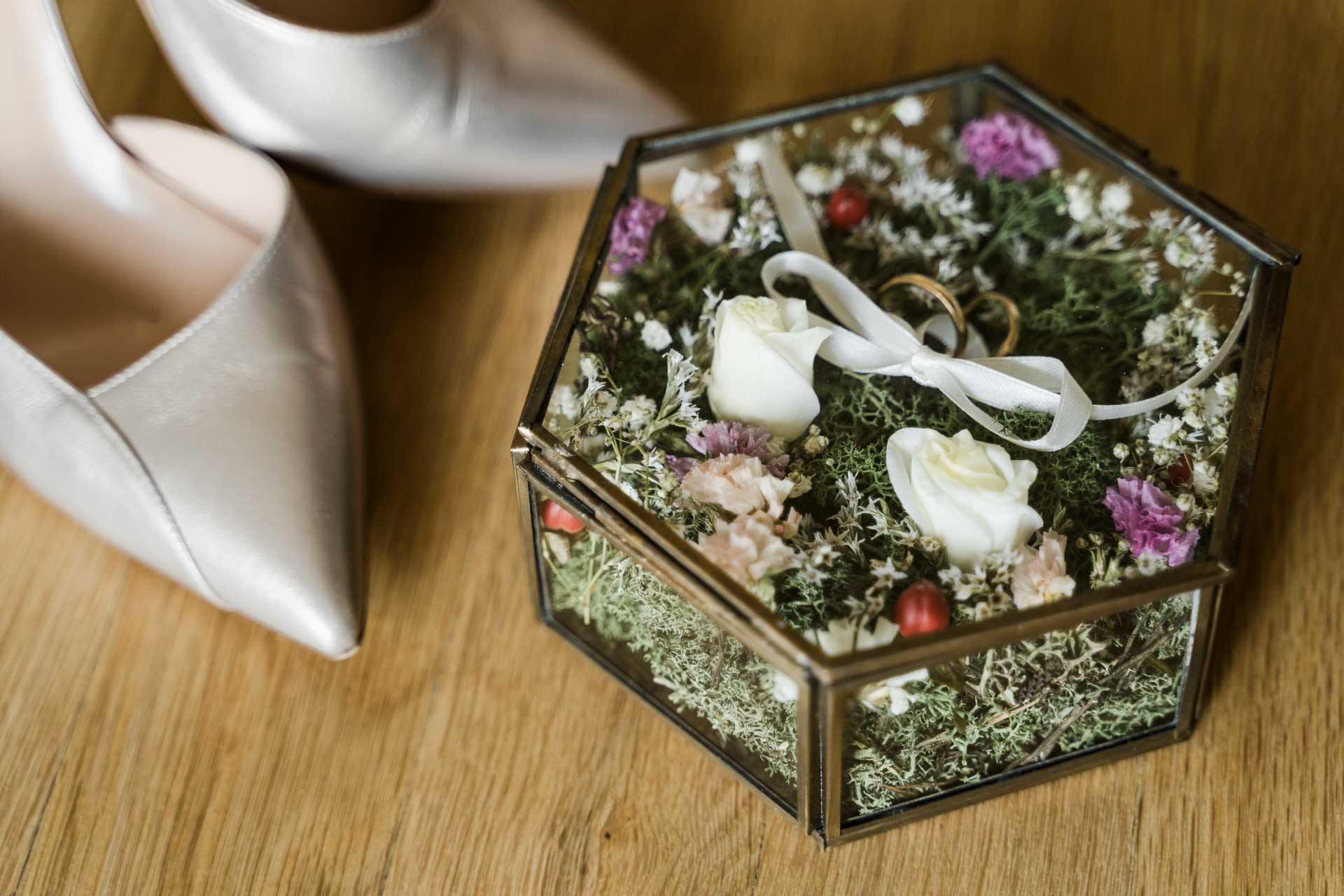 Le scarpe della sposa e la scatola di vetro con le fedi tra i fiori