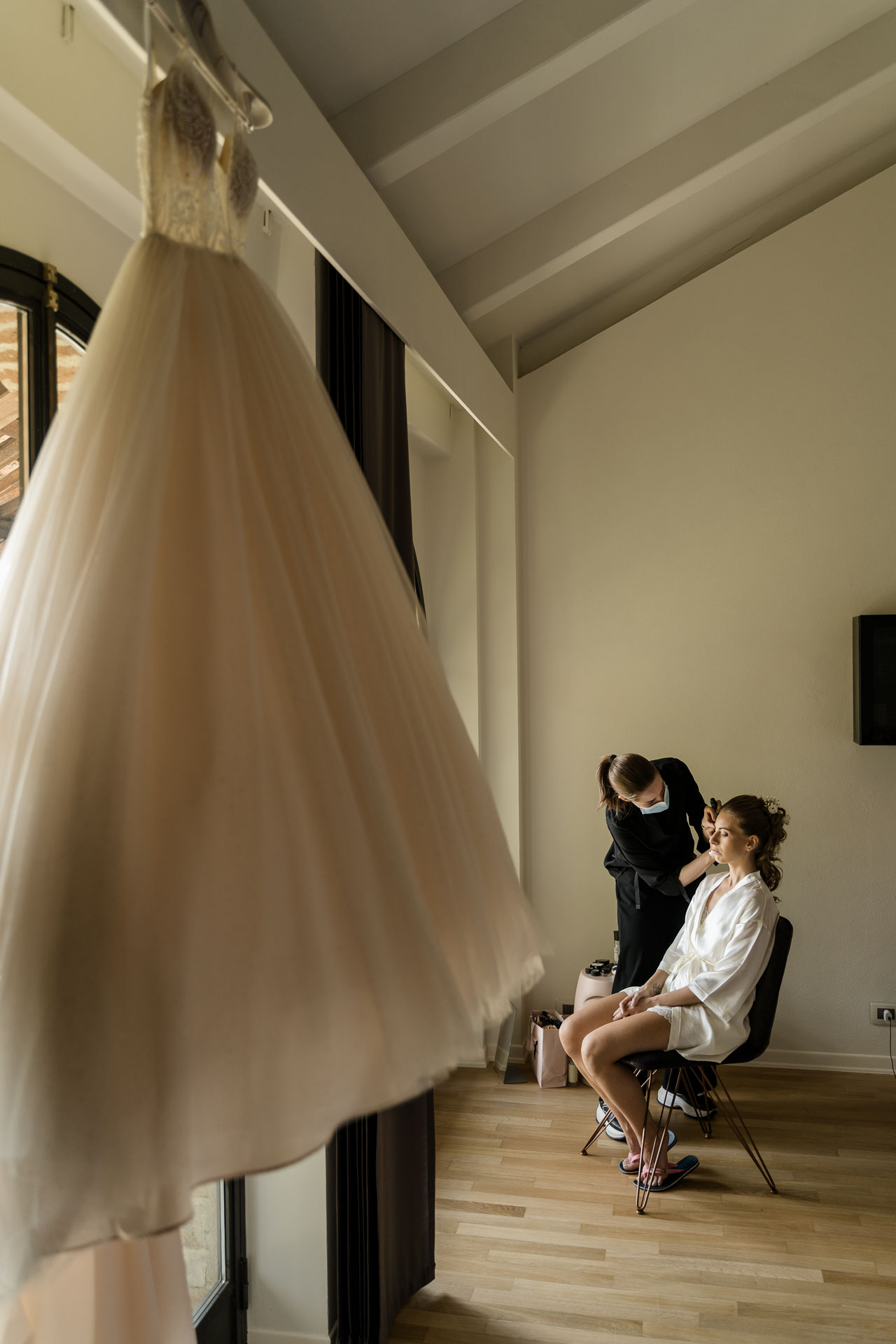 L'abito da sposa appeso e, sullo sfondo, la sposa al trucco