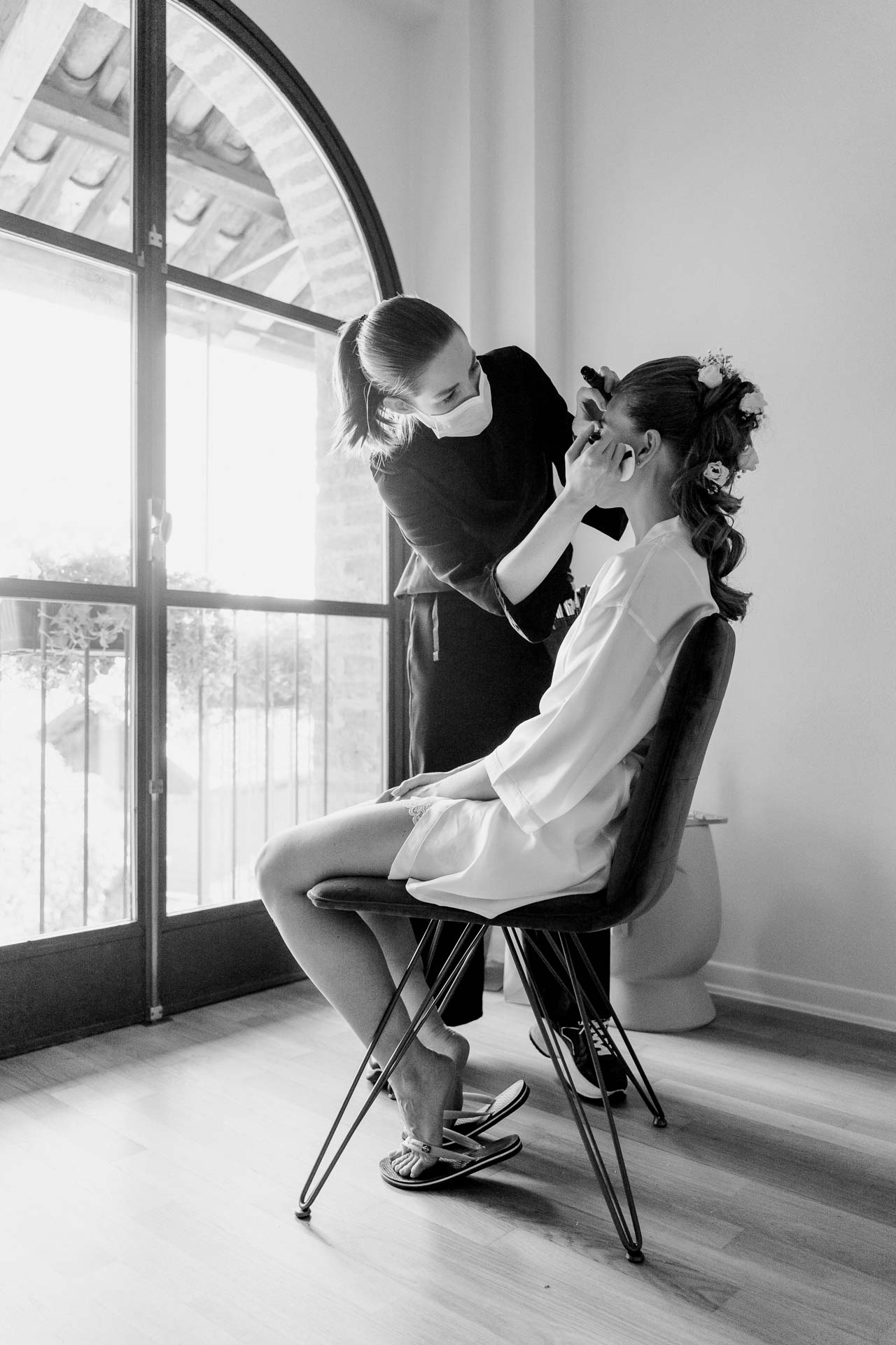 In bianco e nero, la sposa al trucco davanti alla grande finestra ad arco
