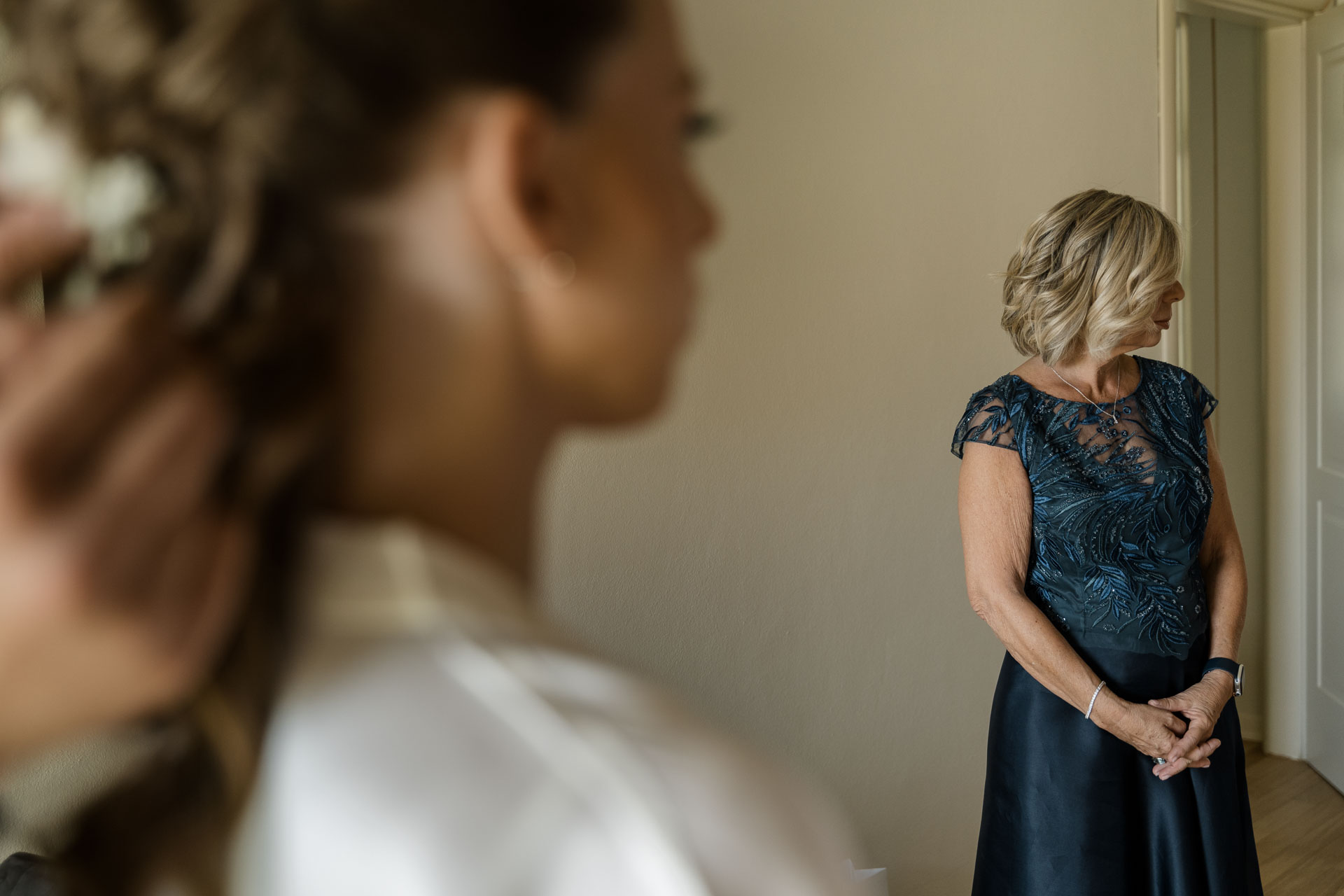 La mamma in abito blu guarda la sposa, ancora in vestaglia