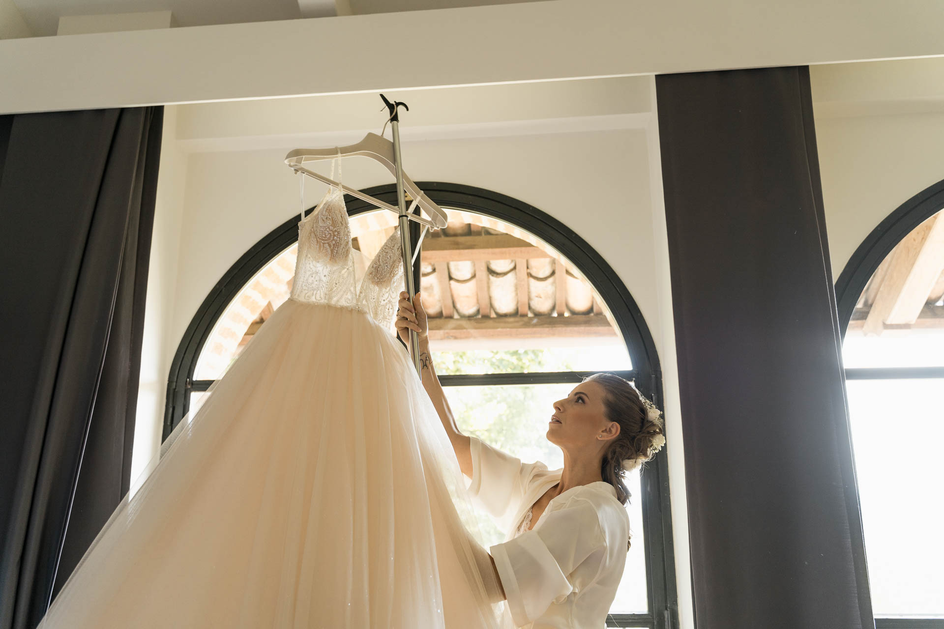 La sposa prende l'abito appeso davanti alle finestre ad arco