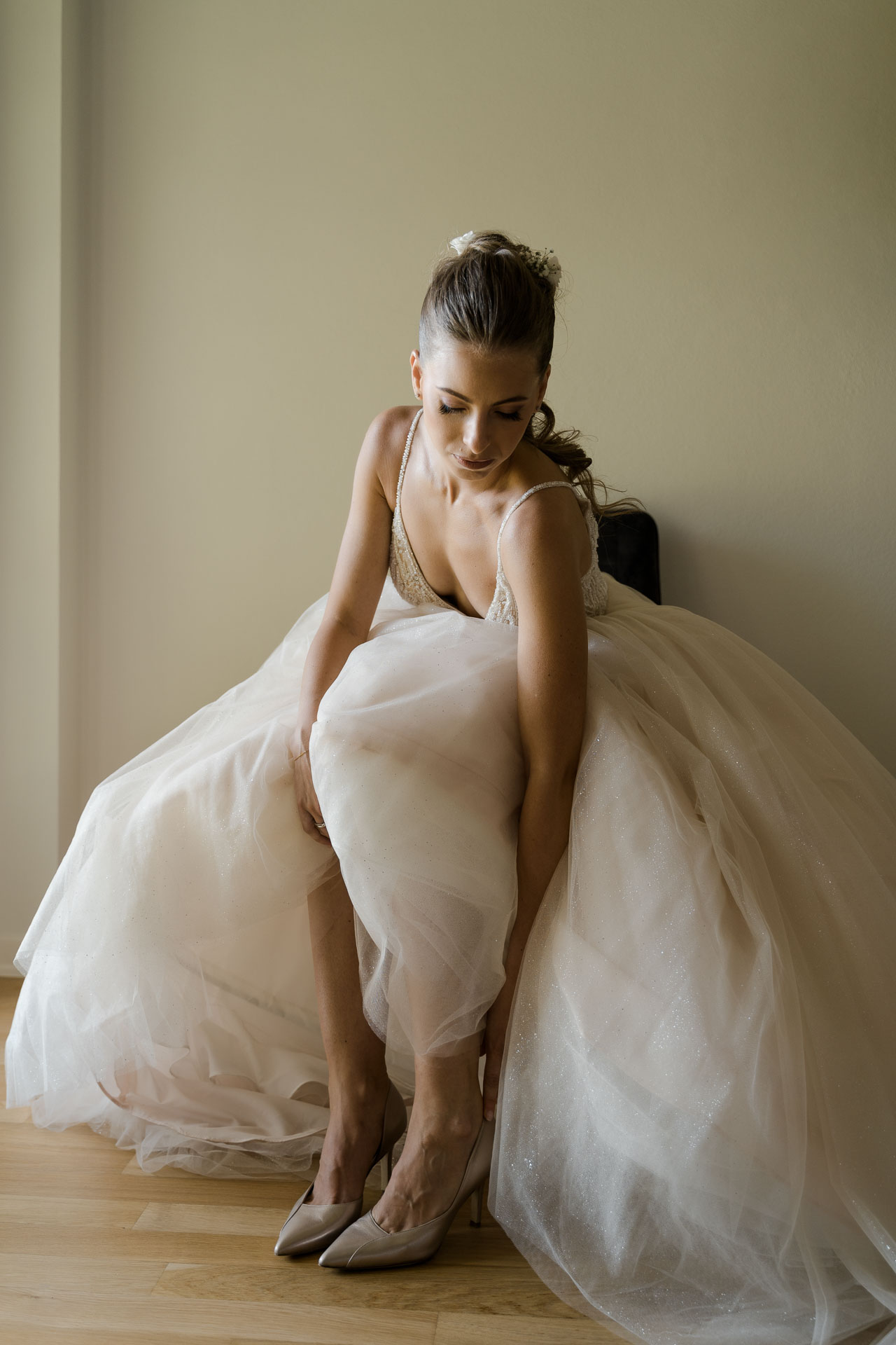 La sposa, seduta, si infila le scarpe con l'abito di tulle intorno