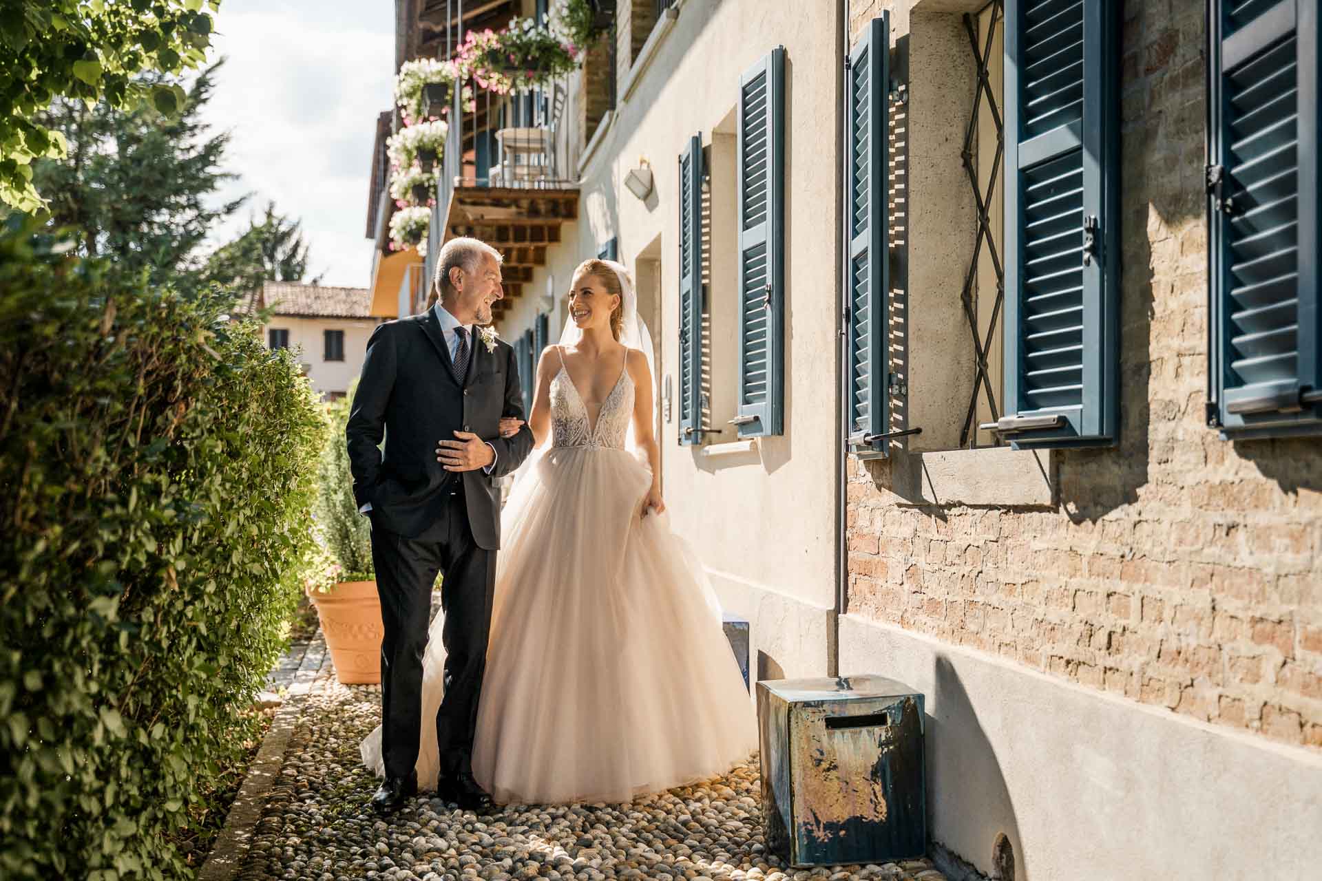 La sposa e il papà lungo la facciata della Madernassa, con le persiane blu