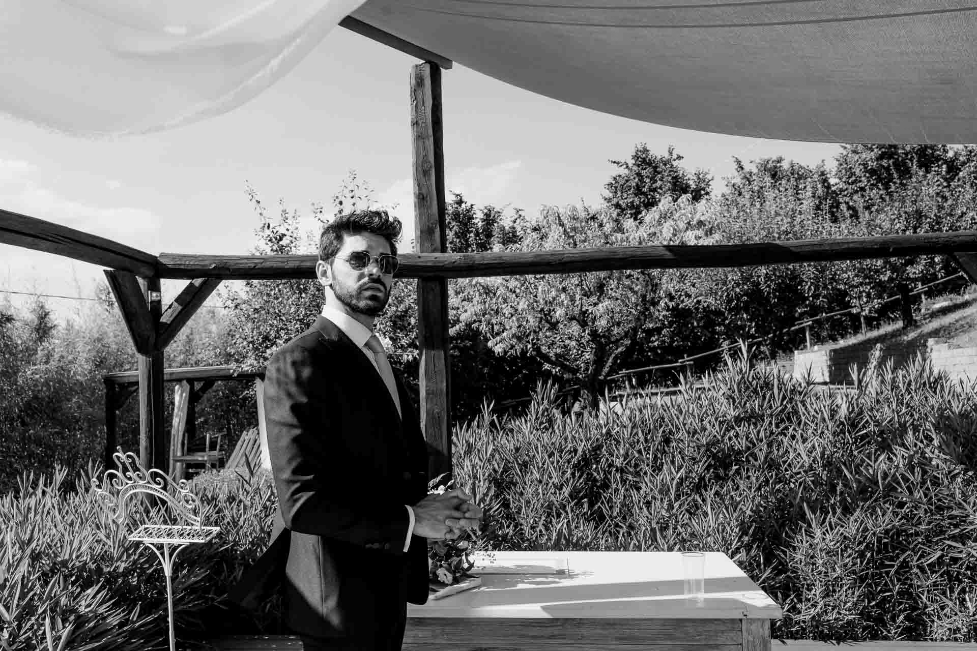 In bianco e nero, lo sposo aspetta al tavolo della cerimonia, nel giardino