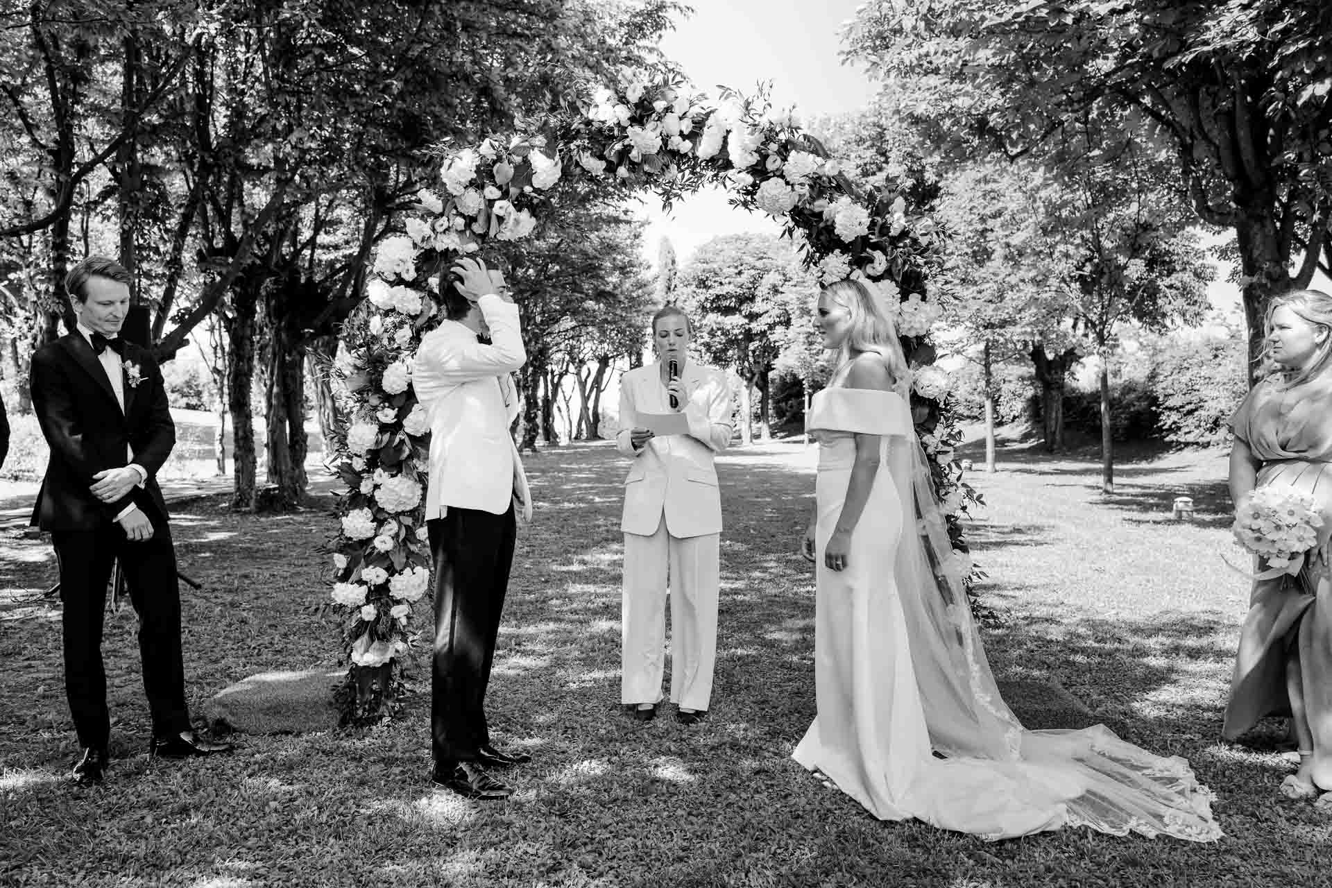 In bianco e nero, la cerimonia sotto l'arco di fiori nel viale d'alberi