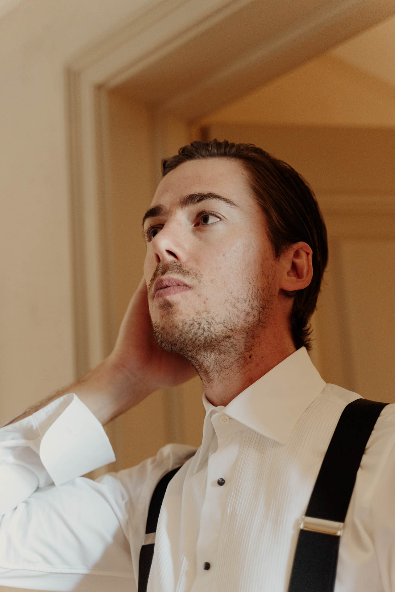 Lo sposo si sistema i capelli, con le bretelle sulla camicia