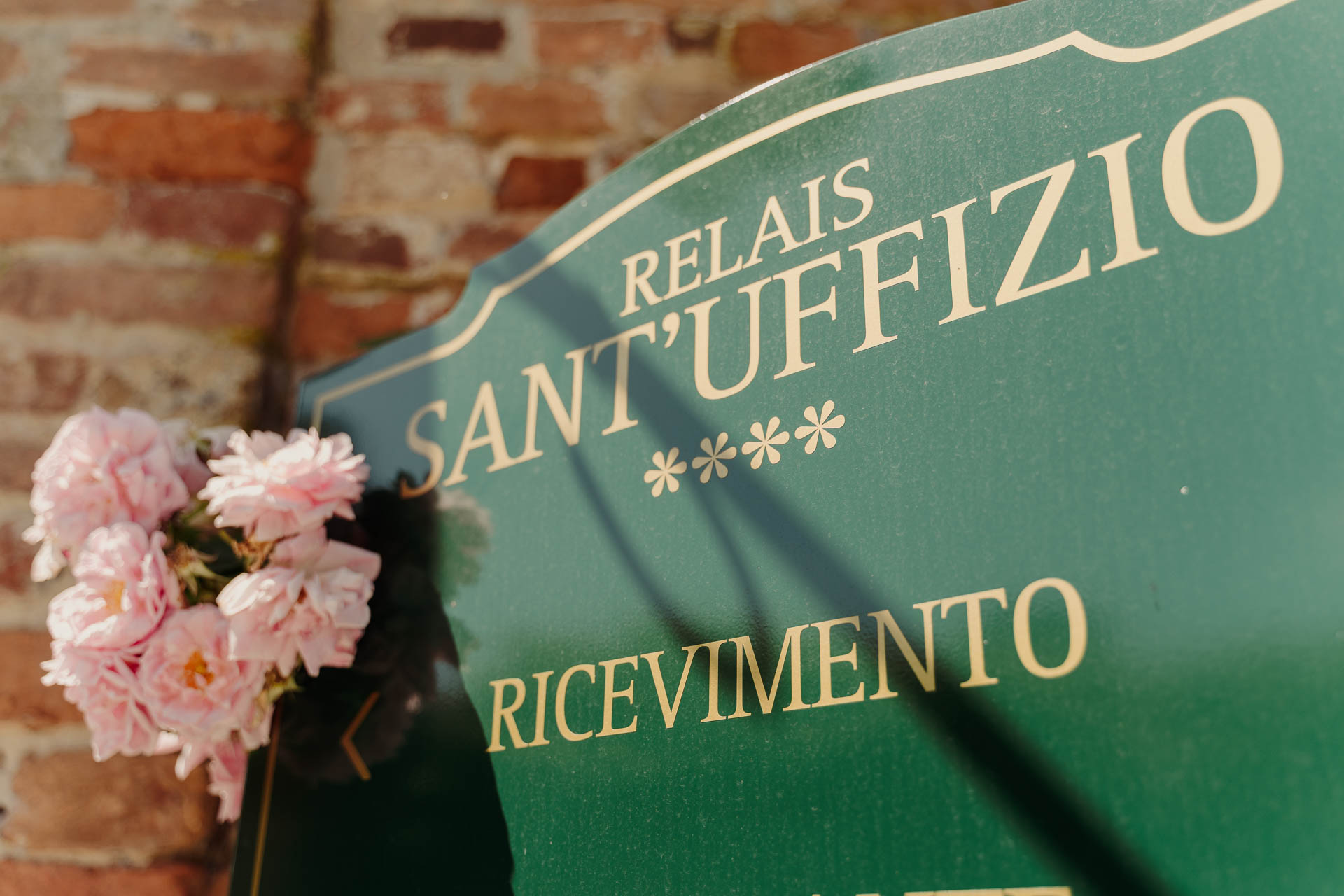 L'insegna del Relais Sant'Uffizio sul muro di mattoni, con le rose rosa