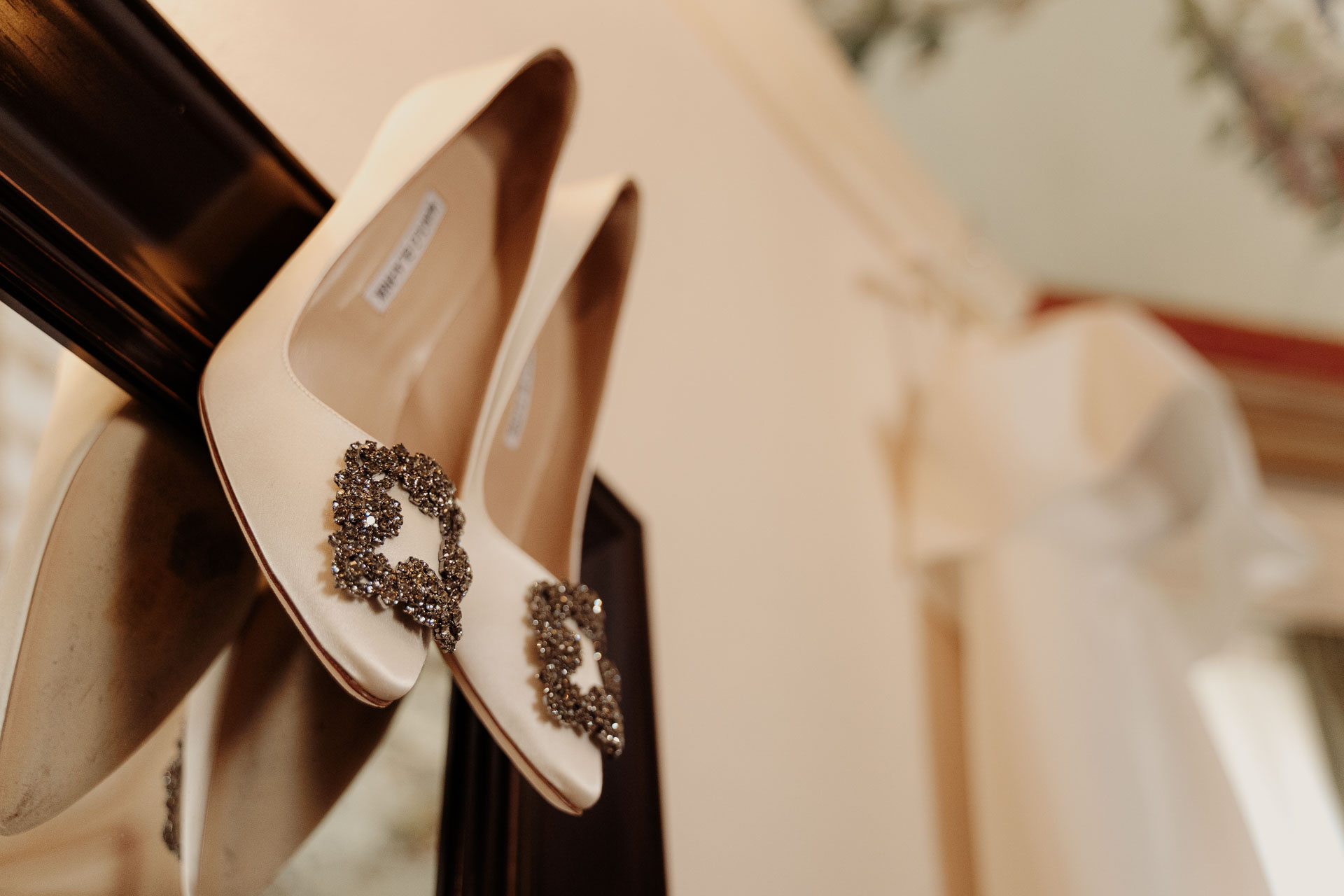Le scarpe della sposa appese, con l'abito sullo sfondo