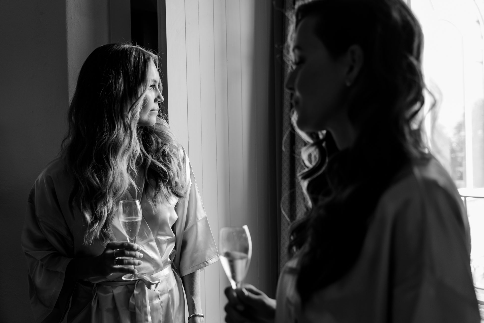 In bianco e nero, la sposa e un'amica con i calici alla finestra