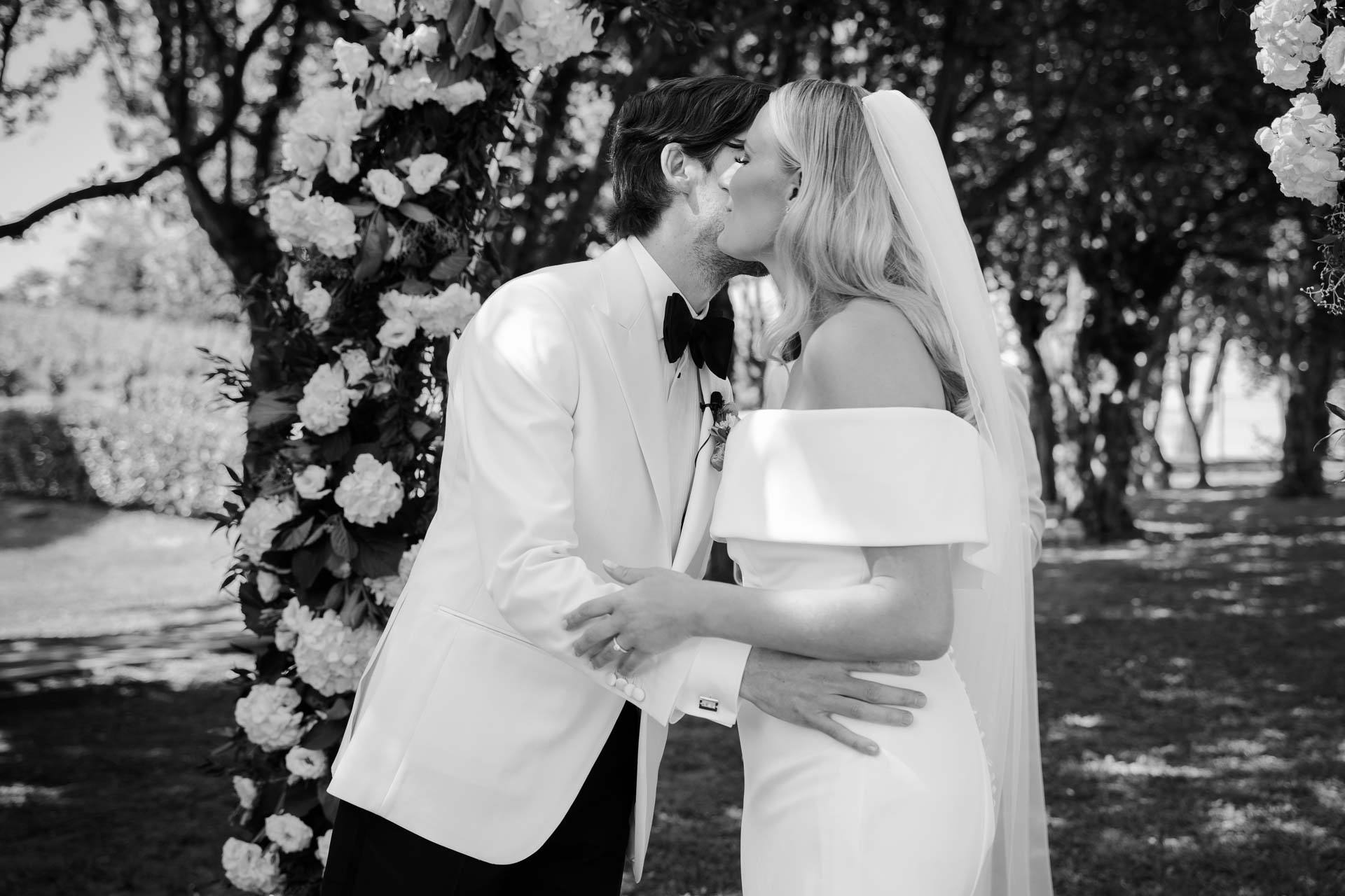 In bianco e nero, il bacio degli sposi sotto l'arco di fiori