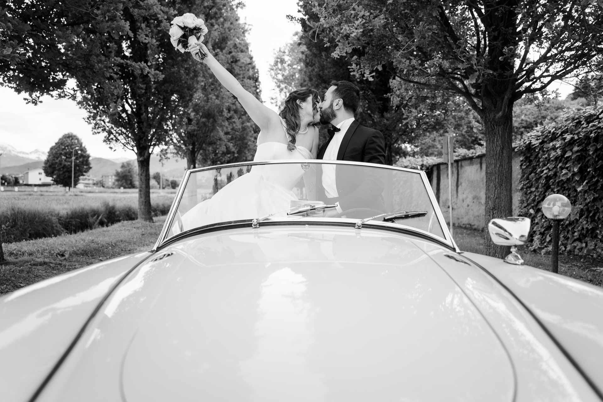In bianco e nero, la sposa alza il bouquet sull'auto nel viale