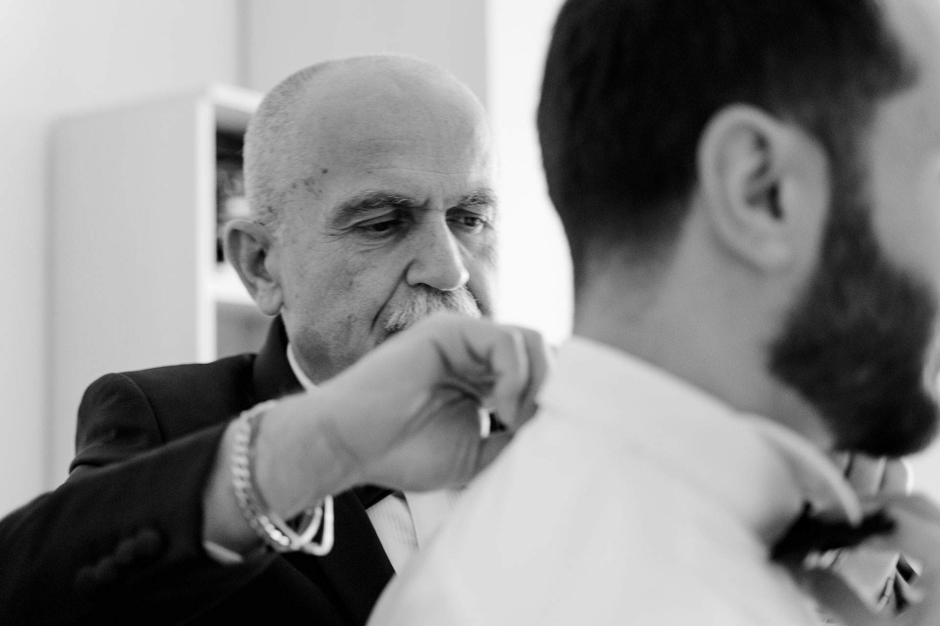 In bianco e nero, un signore sistema il papillon allo sposo