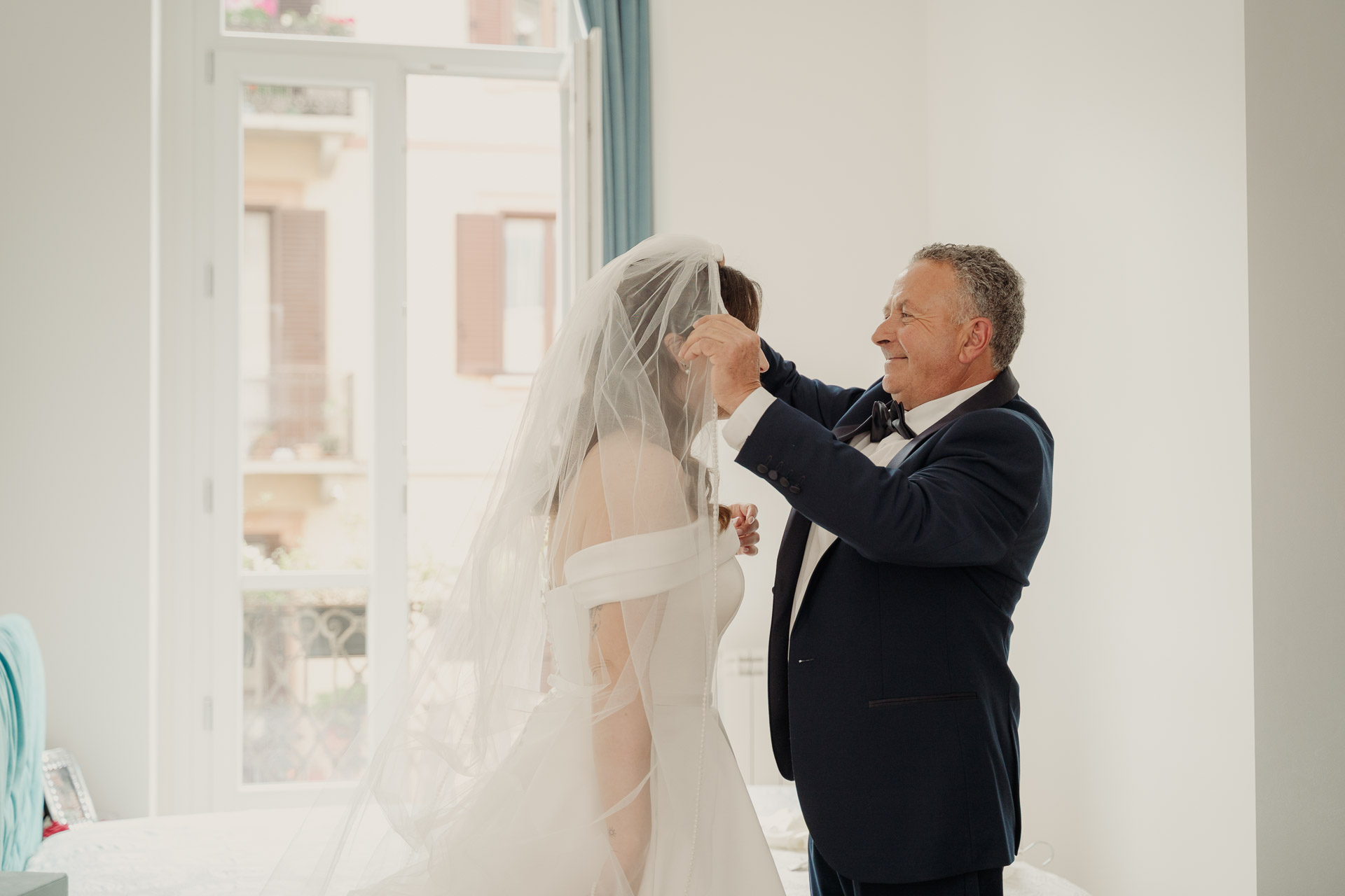 Un signore sistema il velo della sposa davanti alla finestra